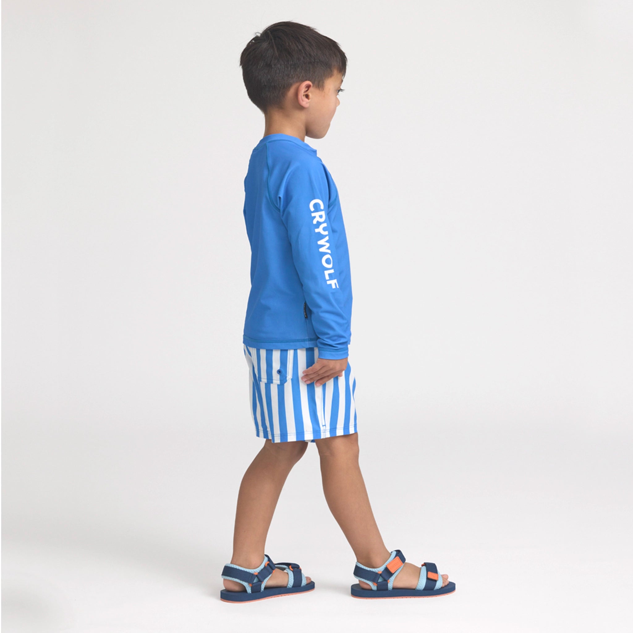 Child wearing a blue long-sleeve shirt with 'Crywolf' branding and striped shorts on a white background