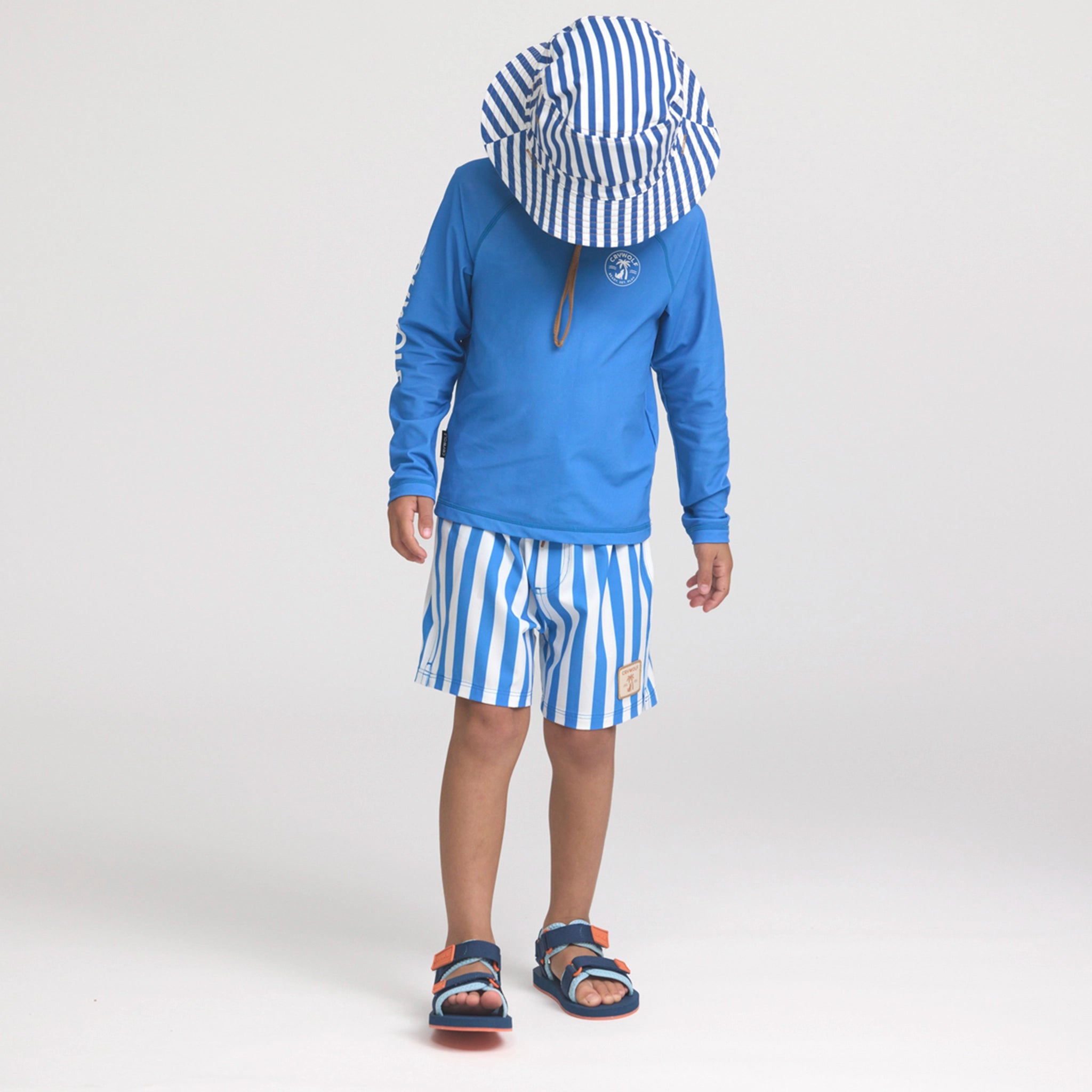 Child wearing a blue long-sleeve shirt and striped shorts with a matching hat on a white background