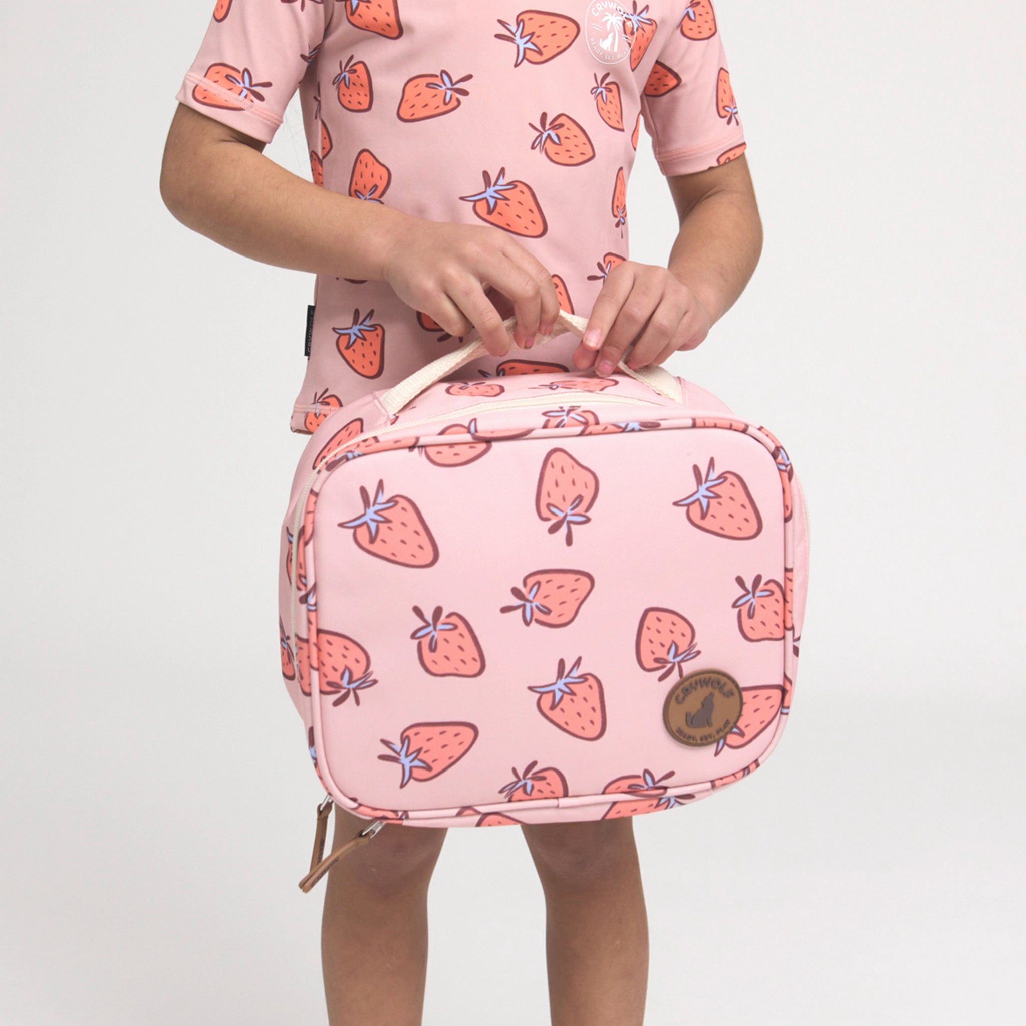 Person holding a pink lunch bag with strawberry pattern against a white background