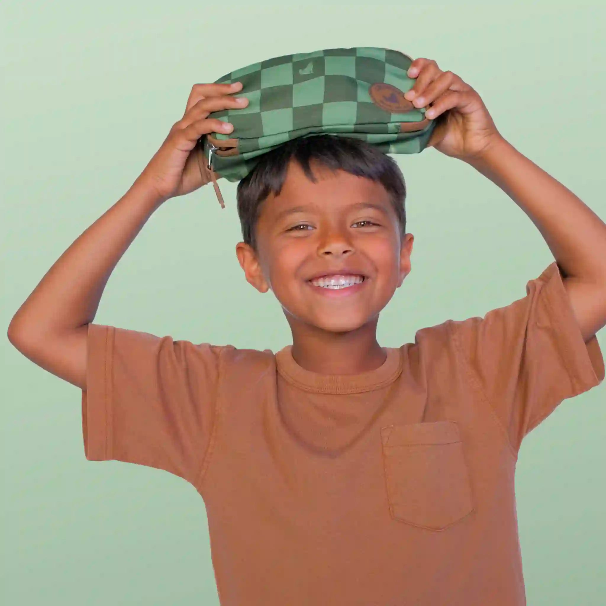 Child holding a green checkered pencil case above their head against a light green background