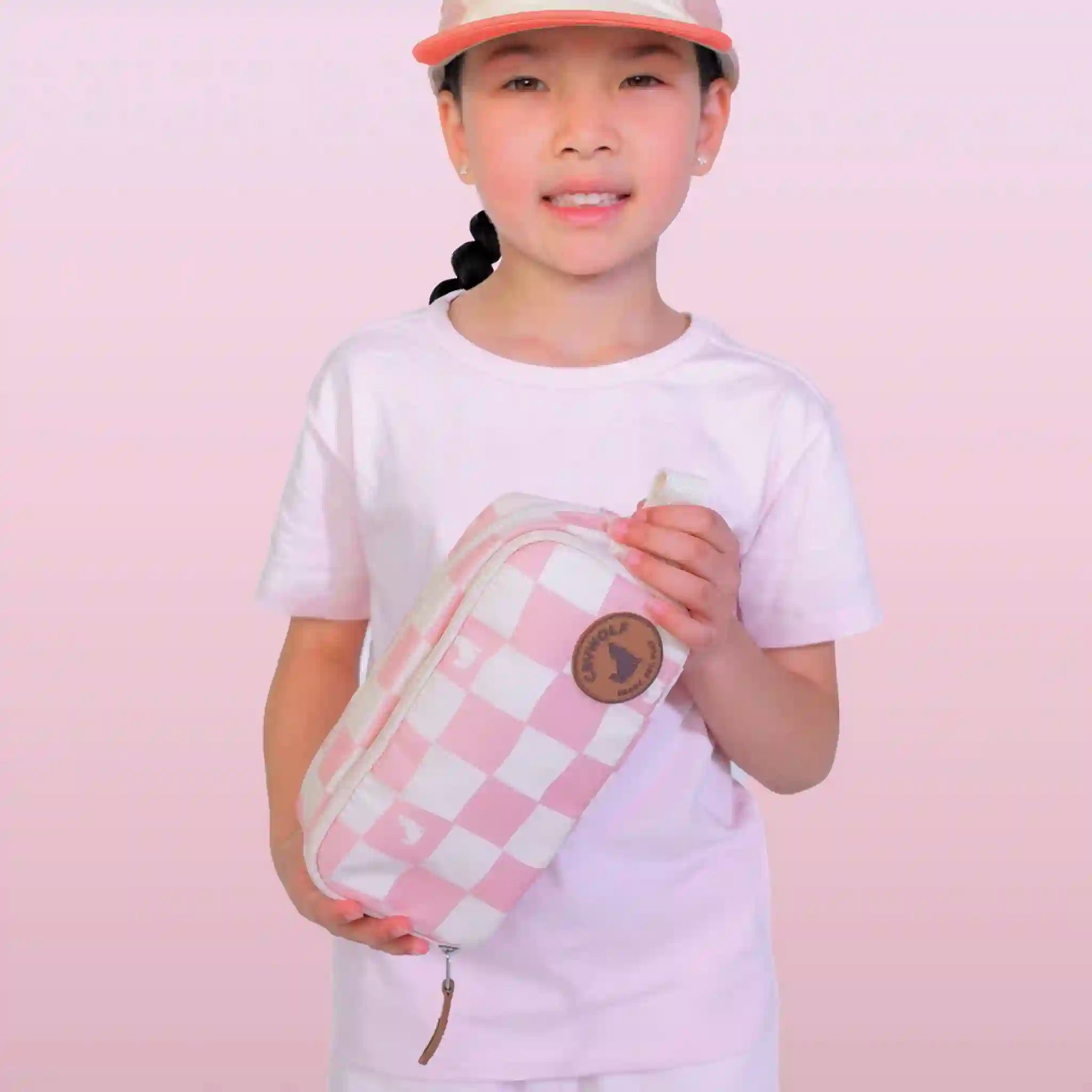 Child holding a pink and white checkered pencil case against a pink background