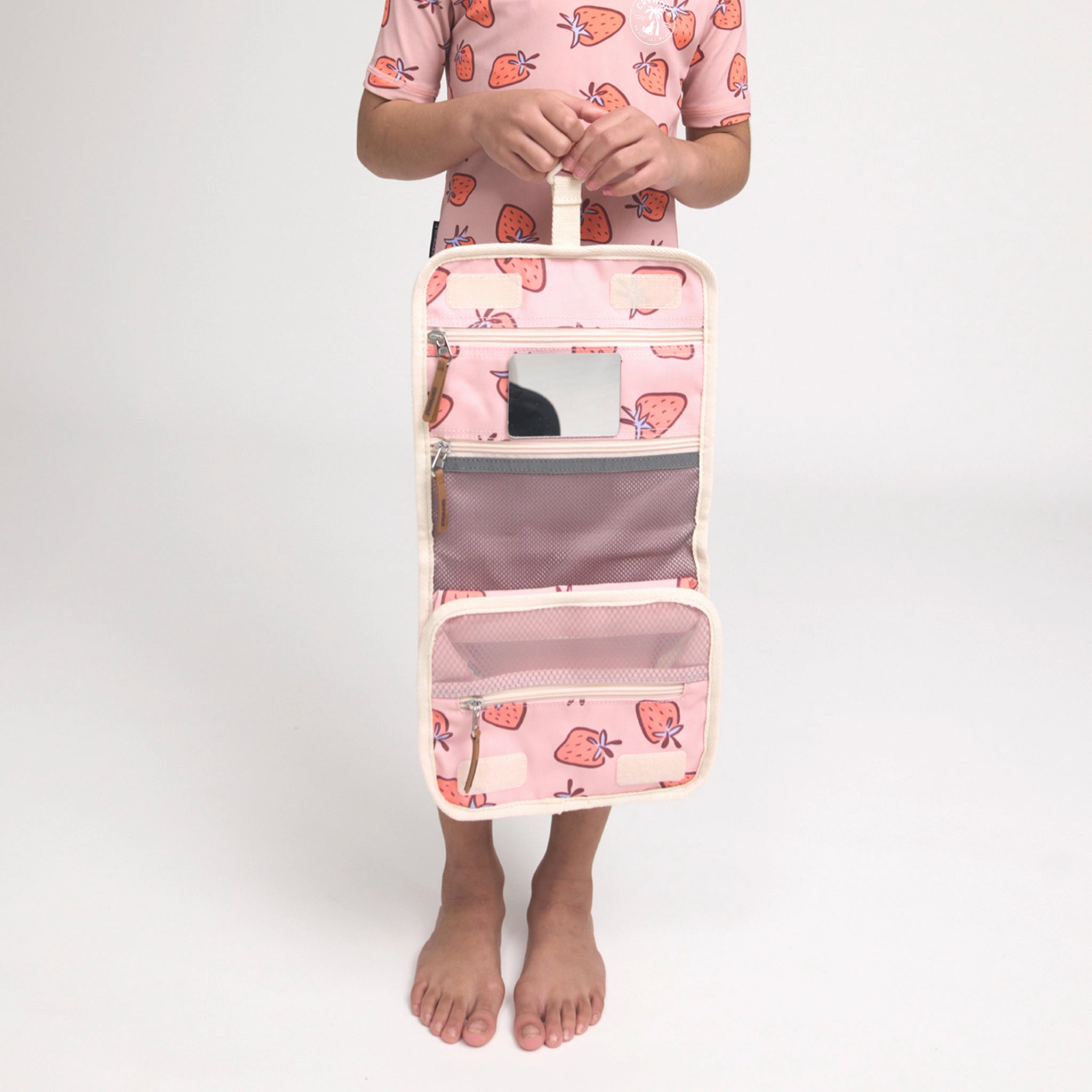 Person holding a pink travel organizer with strawberry pattern on a white background