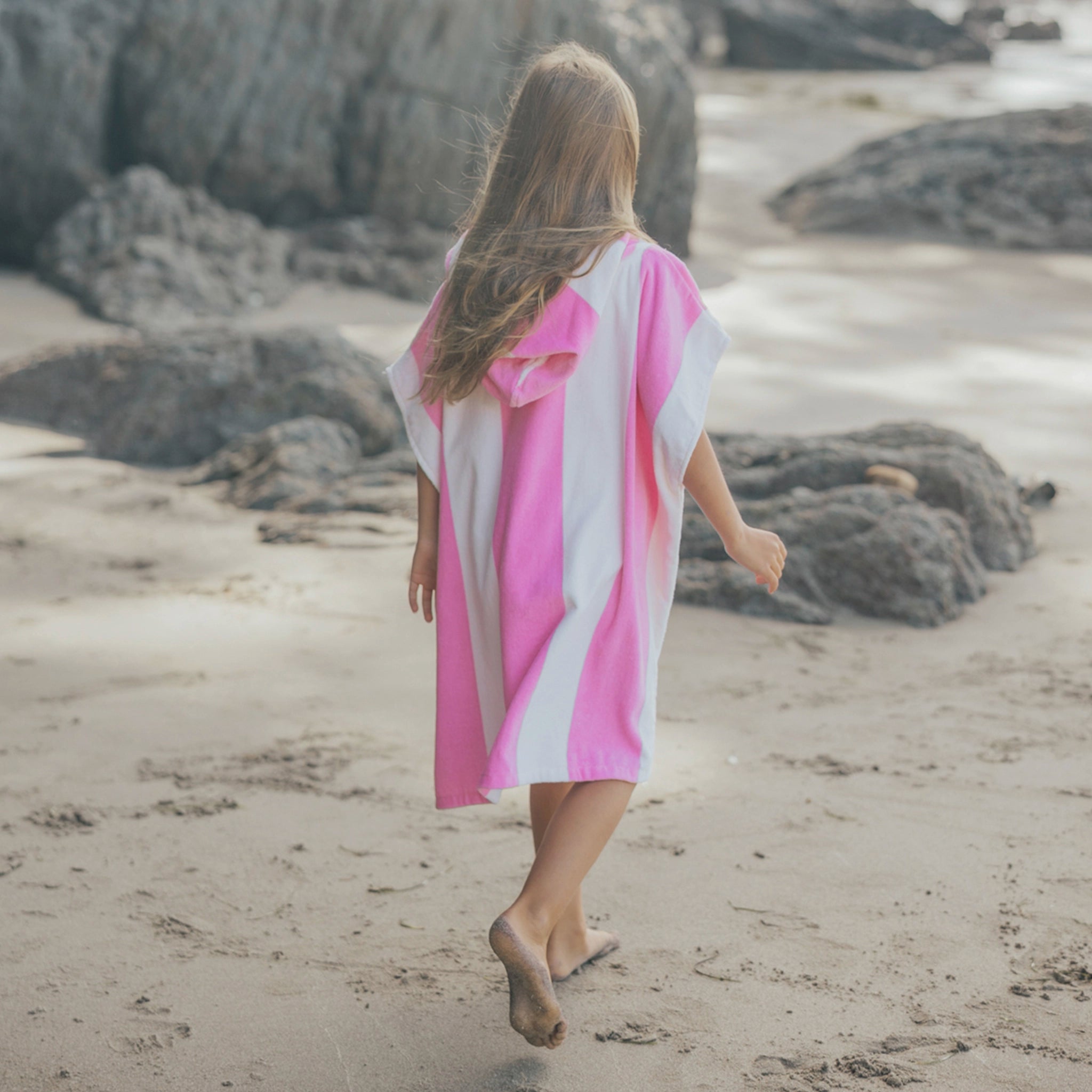 Girl walking on a beach wearing a pink and white towel.