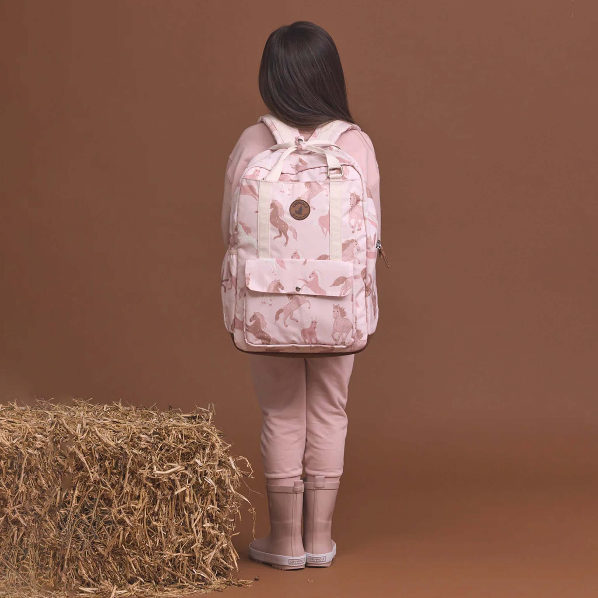 Alt Tag: Crywolf Knapsack - Blush Ponies water-resistant kids backpack with pony print, worn by child, spacious for school travel