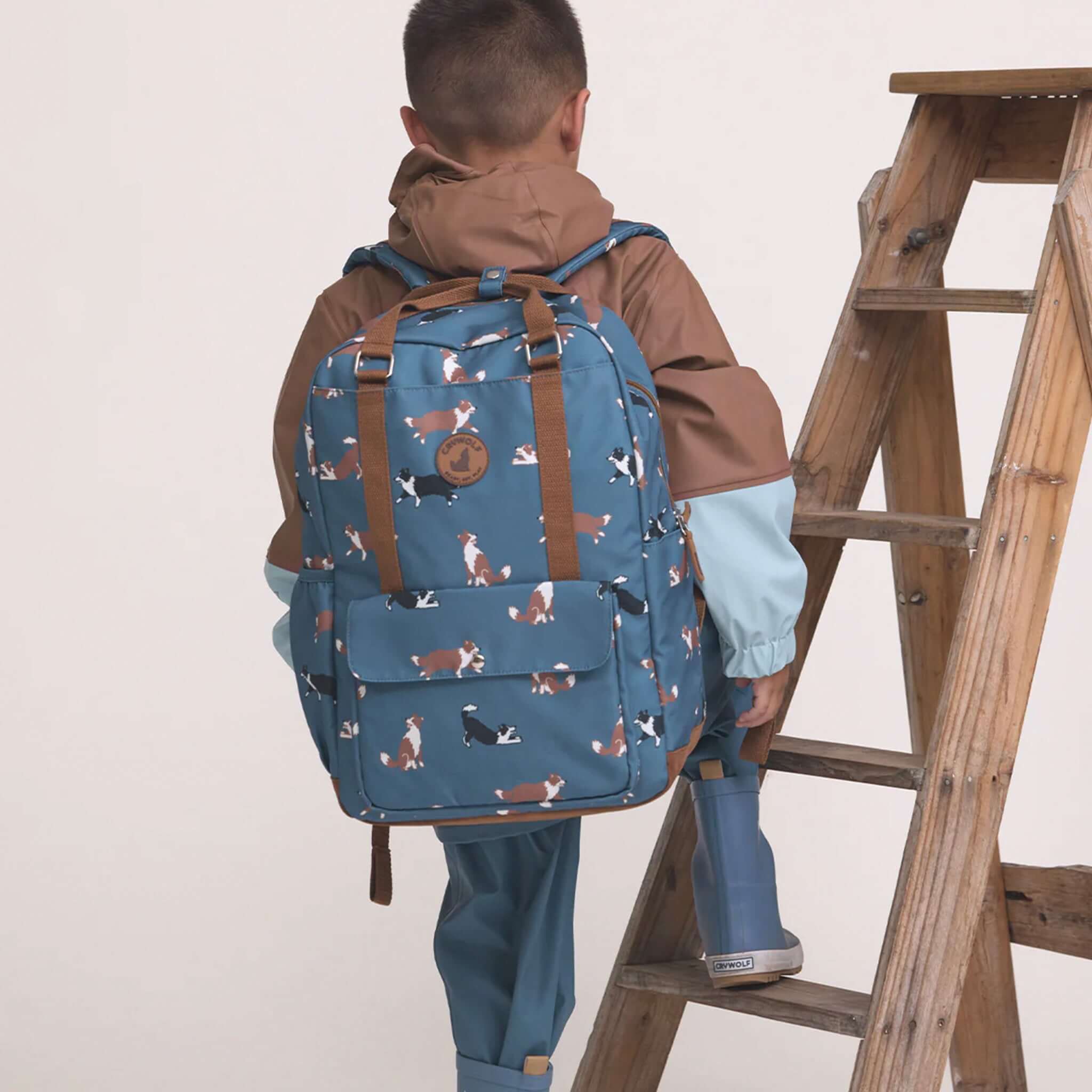 Alt Tag: Crywolf Knapsack - Collies water-resistant kids backpack in blue collie print, worn by child climbing ladder, eco-friendly recycled material