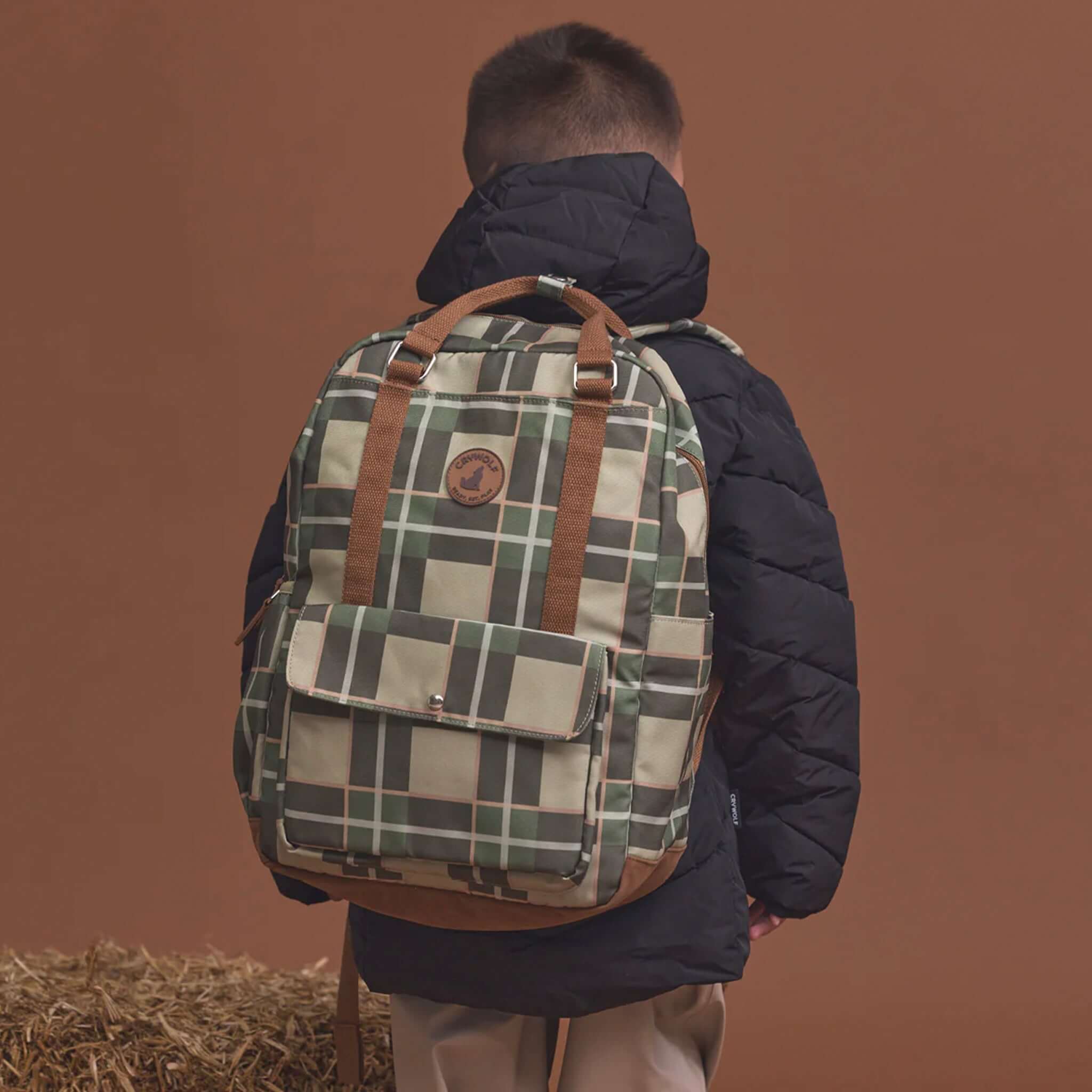 Alt Tag: Crywolf Knapsack - Field Plaid water-resistant kids backpack with plaid print, front pocket and carry straps worn outdoors