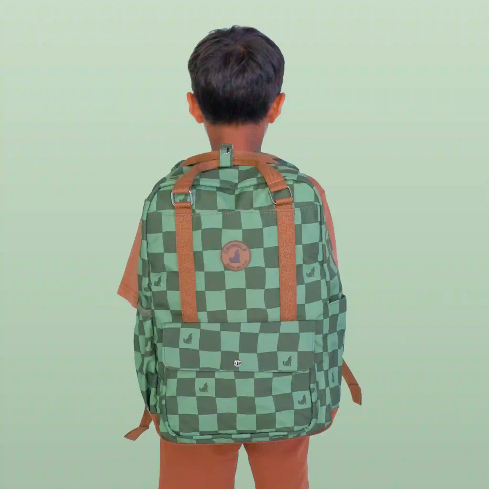 Person wearing a green checkered backpack with brown straps on a light green background