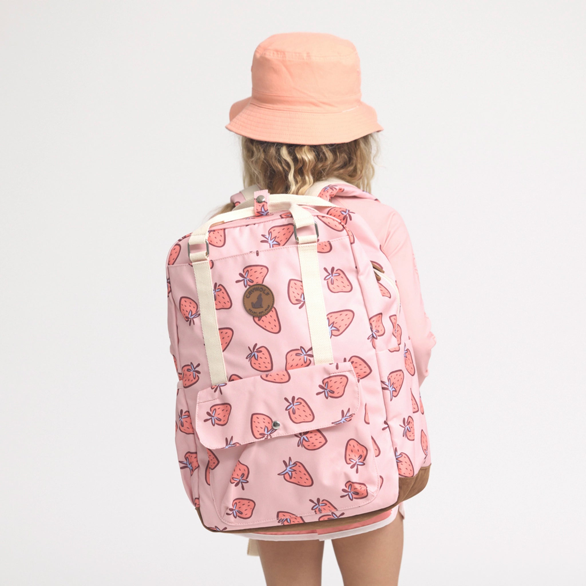 Person wearing a pink backpack with strawberry pattern and a matching hat on a light gray background