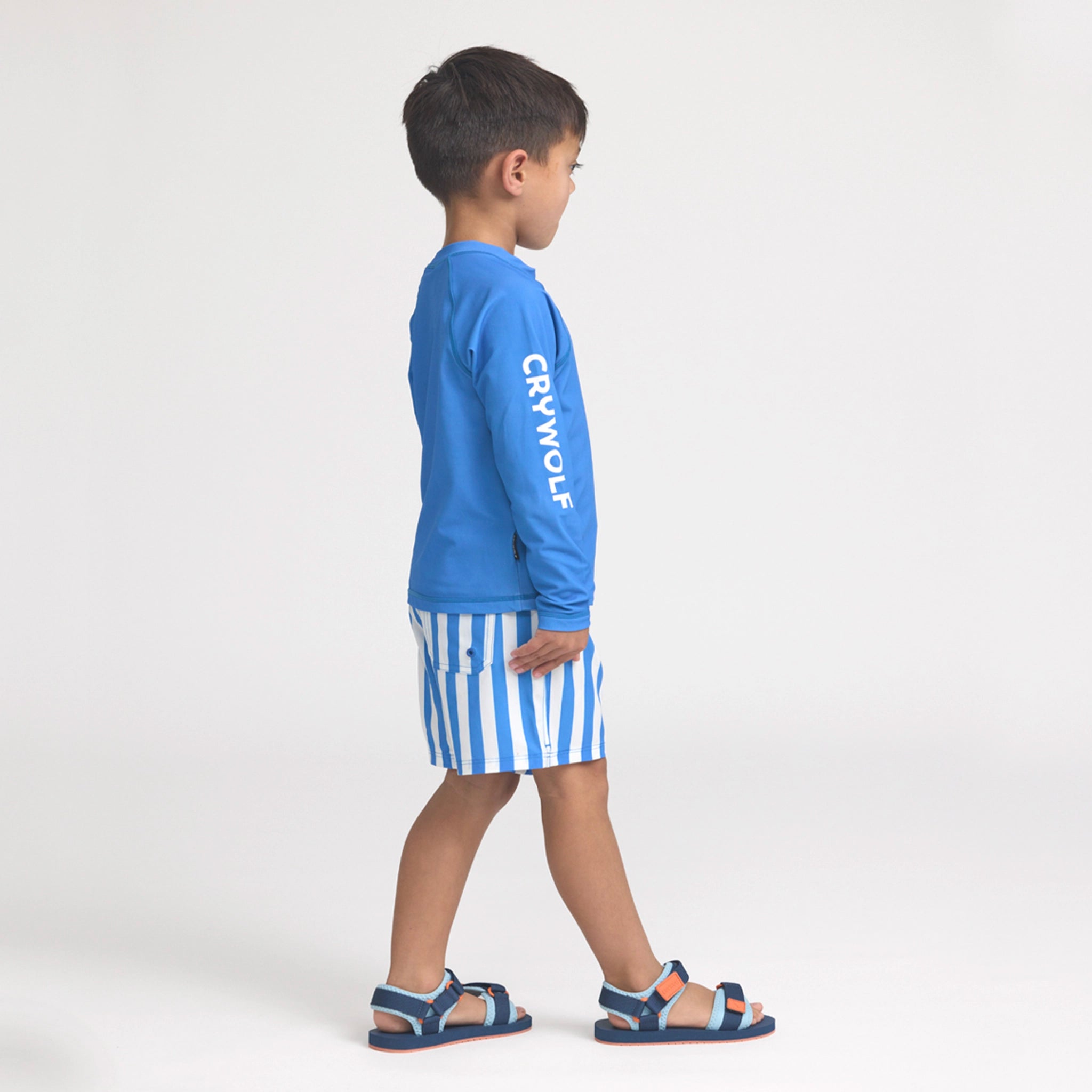 Child wearing a blue long-sleeve rash vest with 'Crywolf' branding and striped shorts on a white background