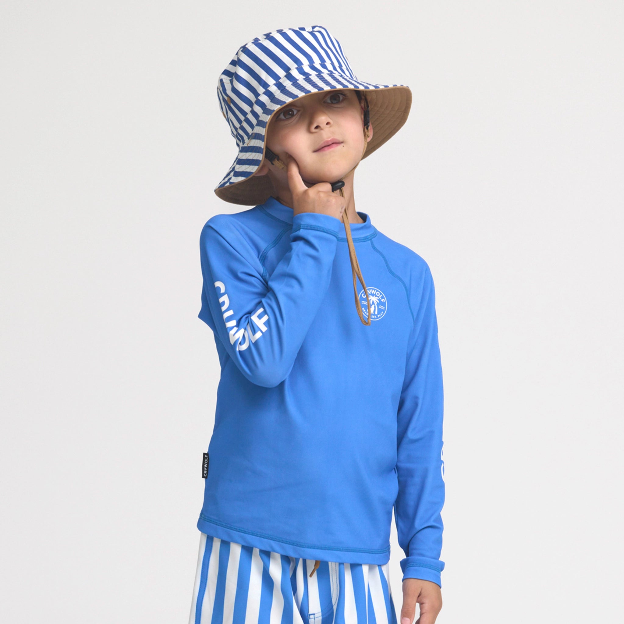 Child wearing a blue long-sleeve rash vest and striped hat on a light gray background