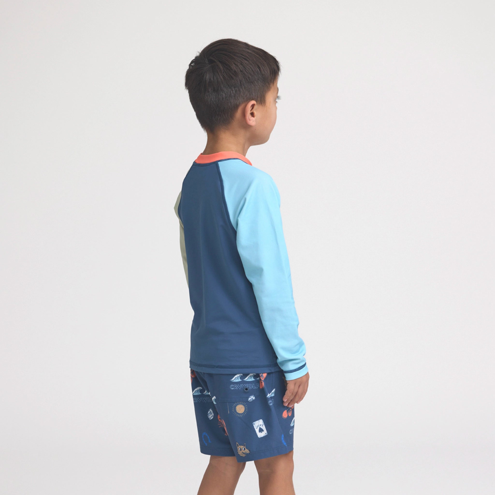 Child wearing a blue and light blue long-sleeve rash vest with patterned shorts on a white background