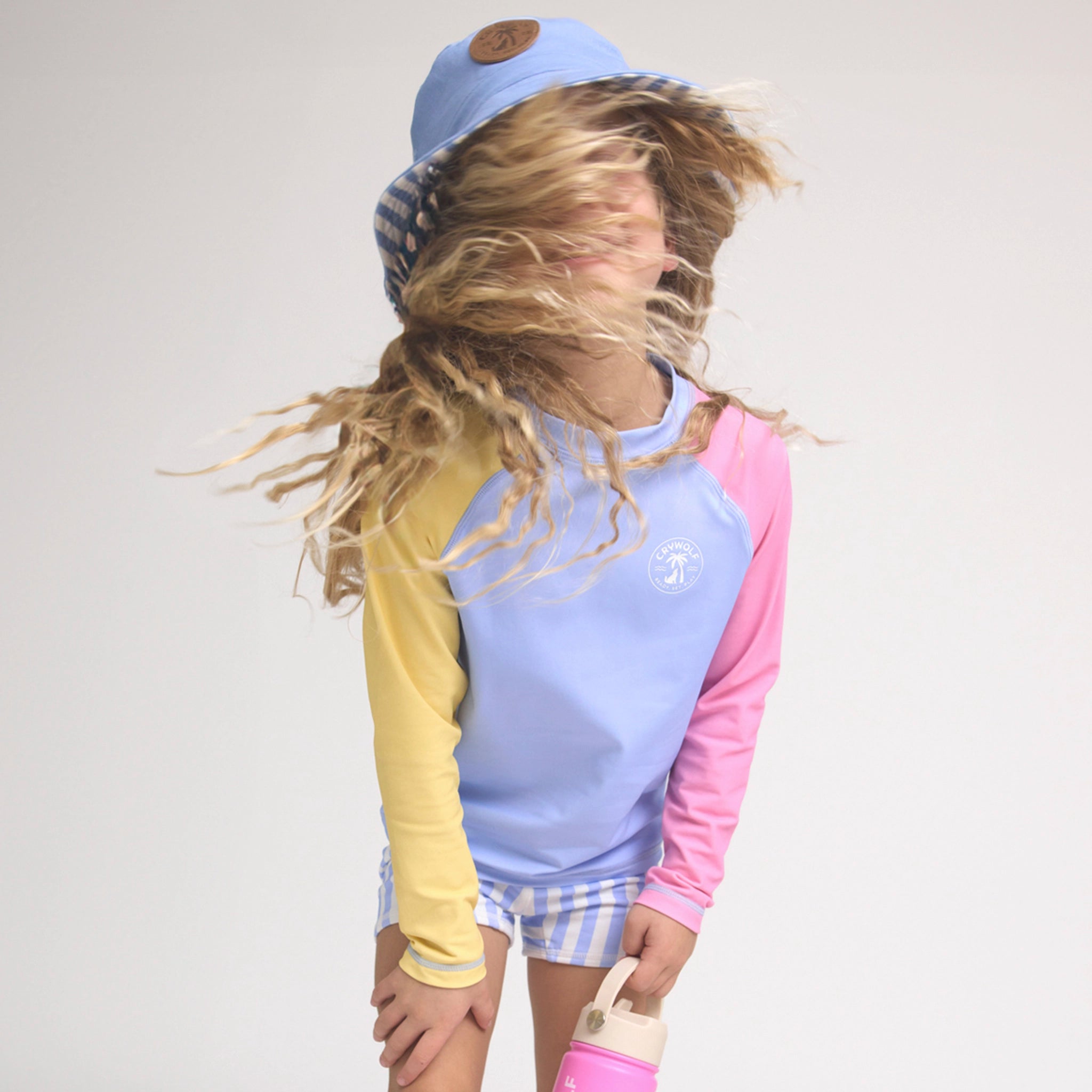 Child wearing a colorful rash vest with a light blue hat on a plain background