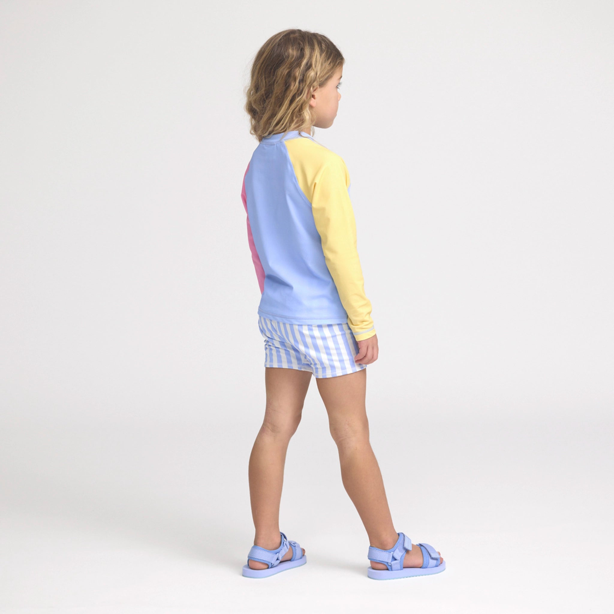 Person wearing a colorful rash vest with a light blue and yellow top and checkered shorts on a white background