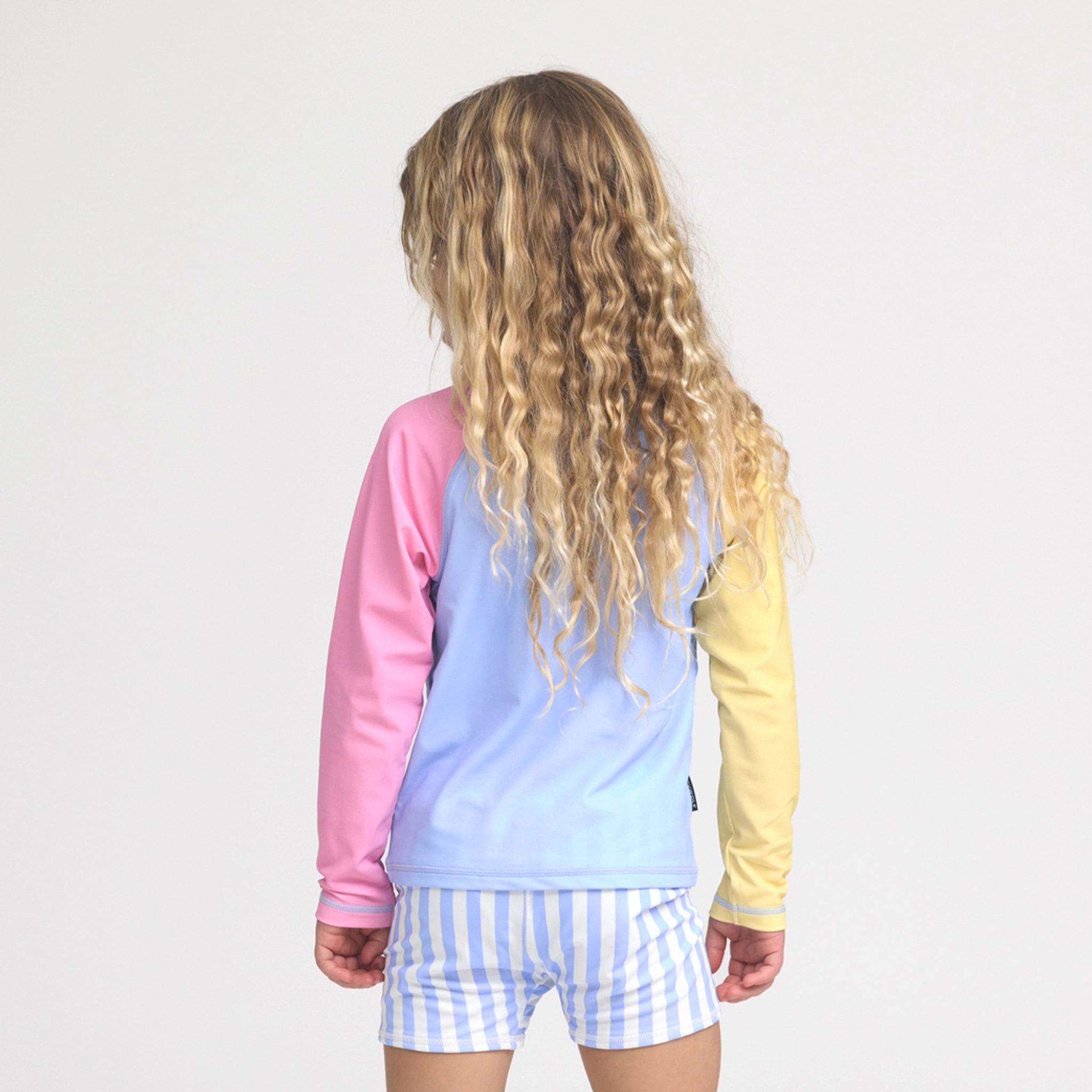 Person wearing a colorful rash vest with a light blue and yellow top and checkered shorts on a white background