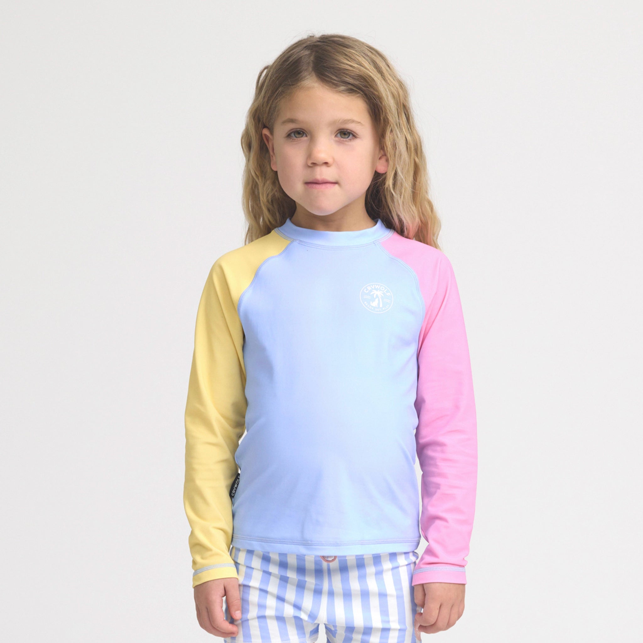 Person wearing a colorful rash vest with a light blue and yellow top and checkered shorts on a white background