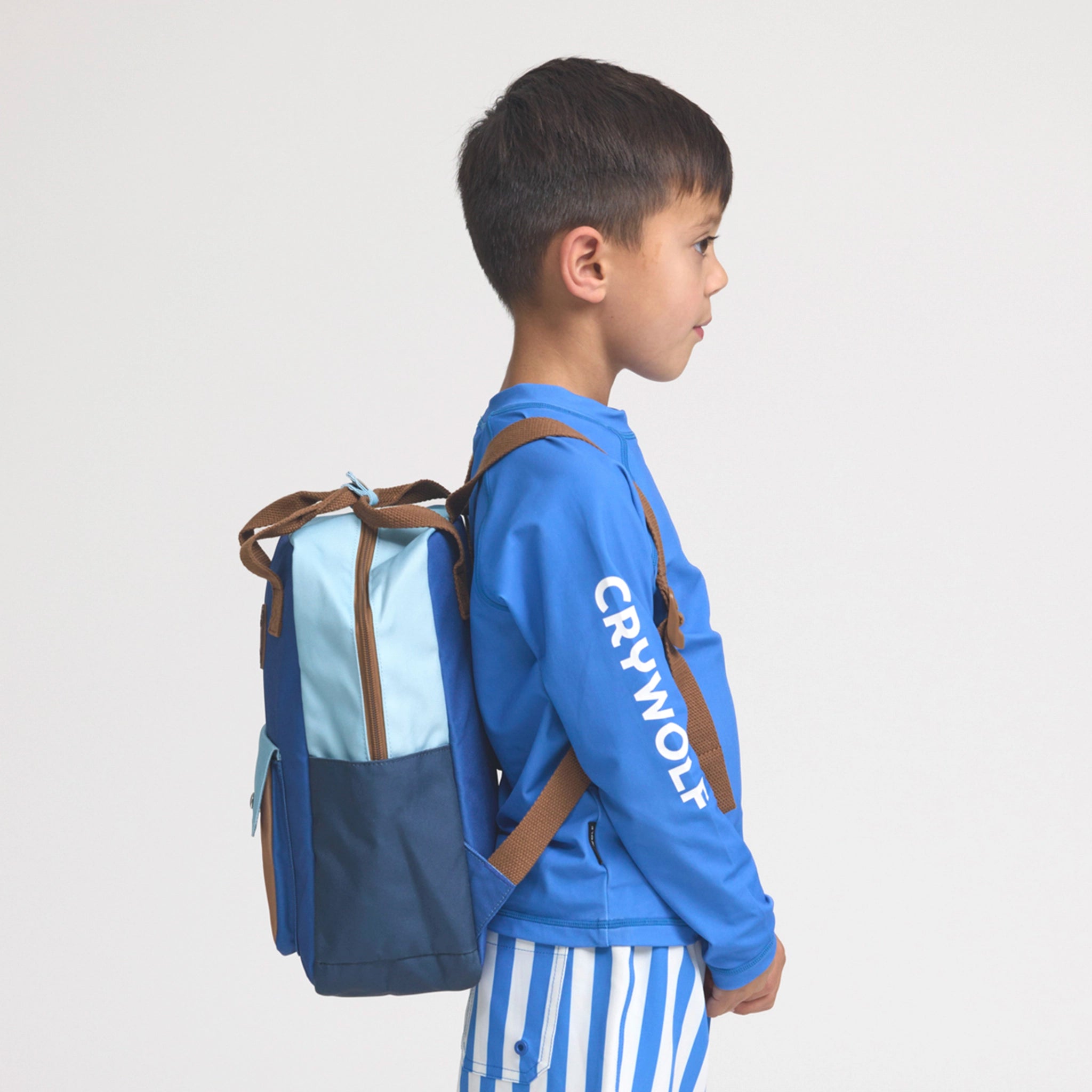 Child wearing a blue jacket with 'Crywolf' branding and a two-toned backpack on a light gray background