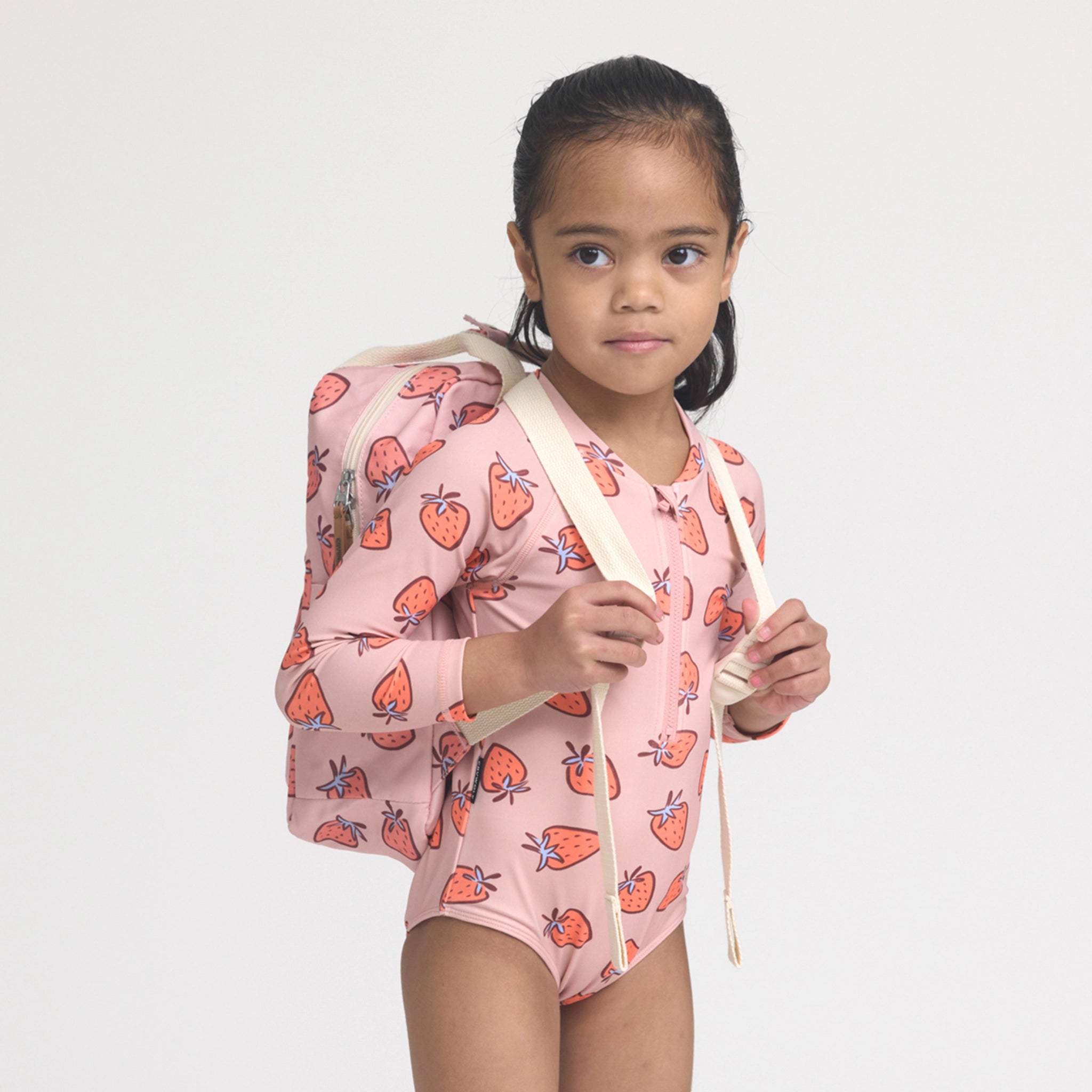Young girl wearing a pink swimsuit with strawberry pattern on a plain background