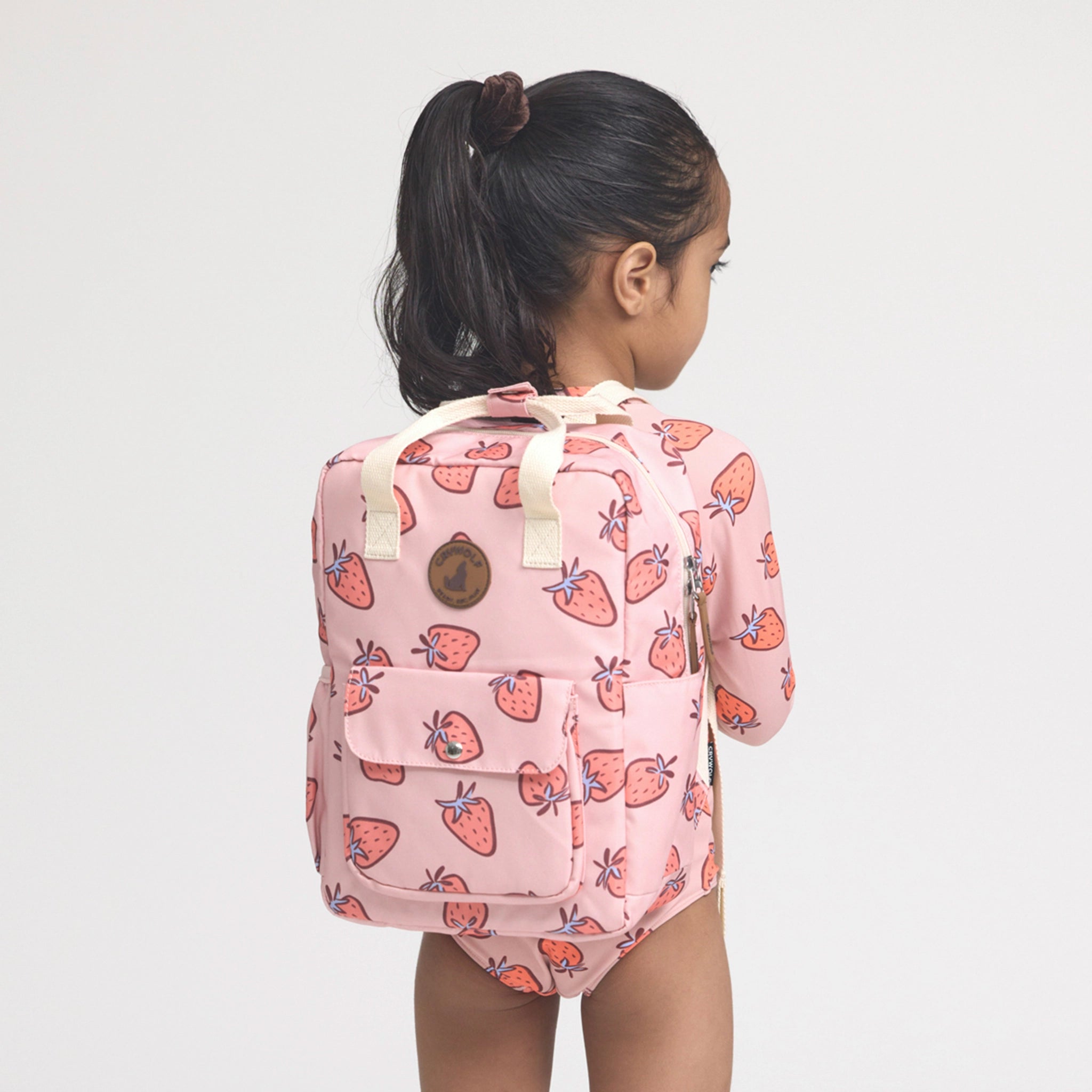 Child wearing a pink backpack with strawberry pattern on a plain background