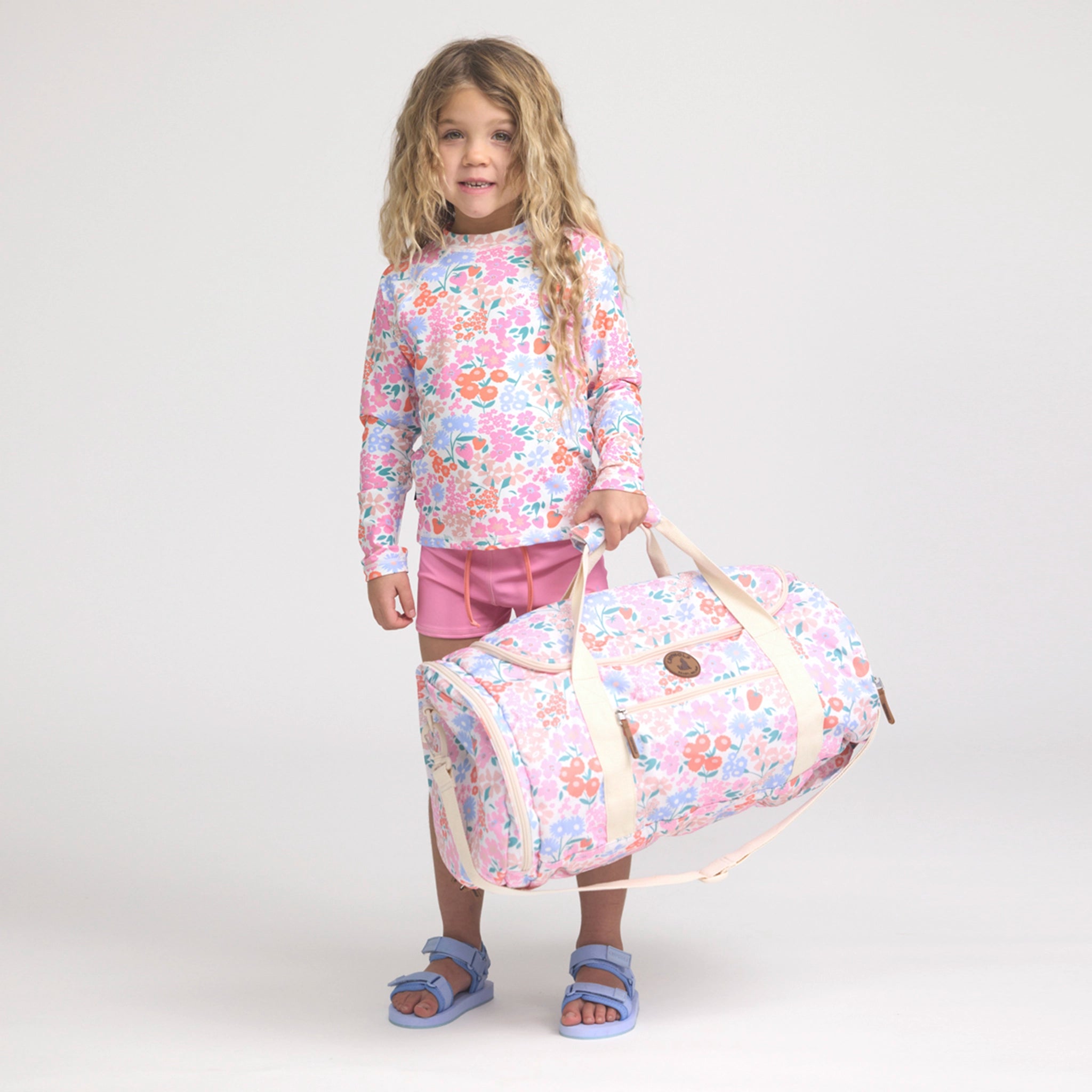 Child holding a floral-patterned bag against a white background