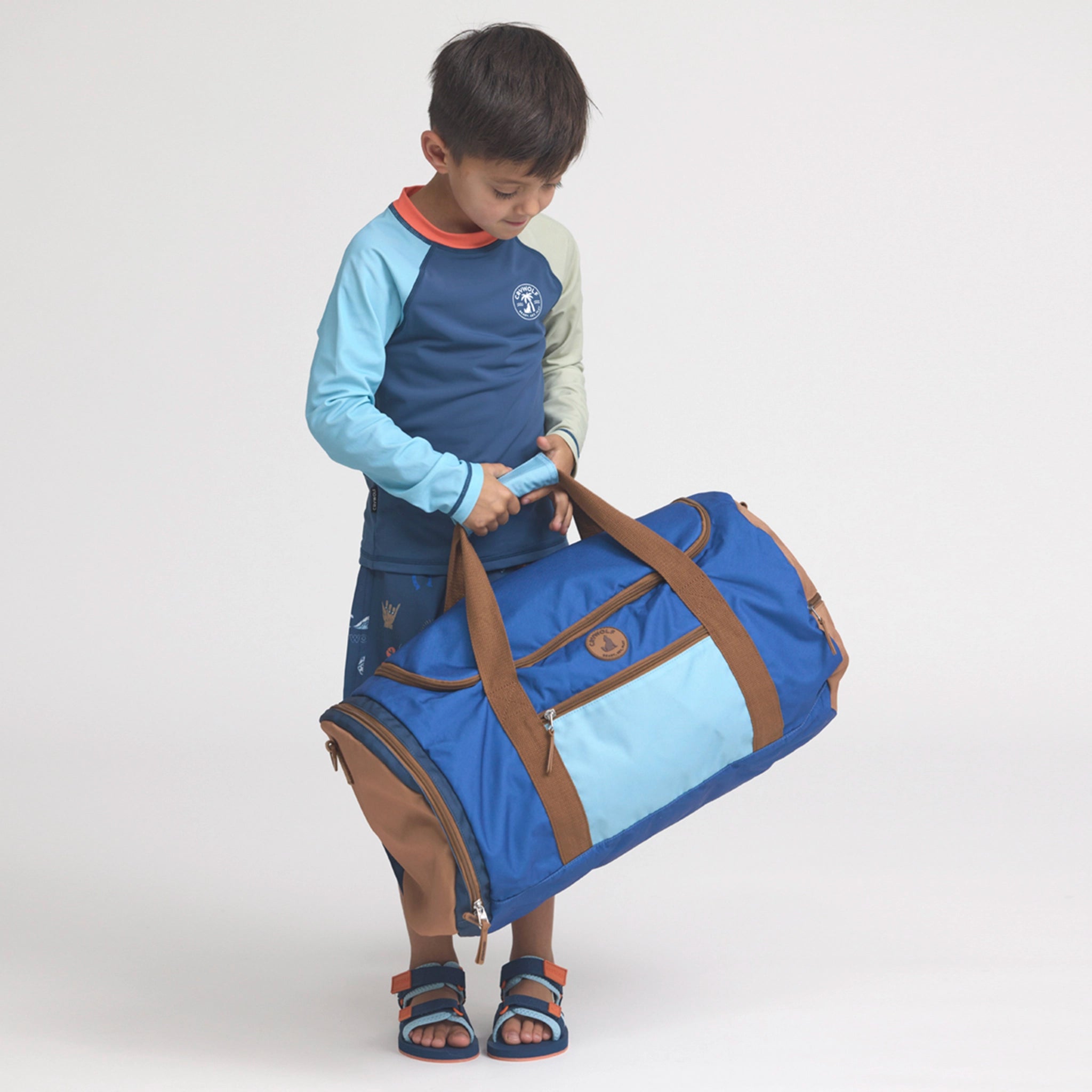 Child holding a blue and brown duffel bag on a white background