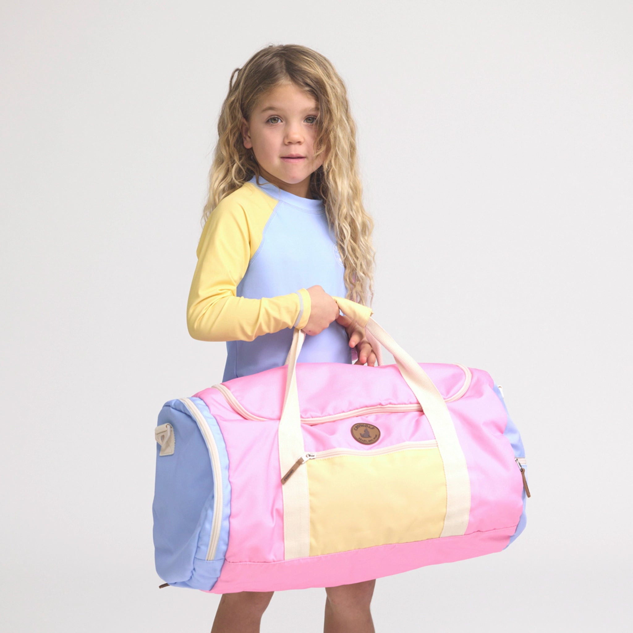 Young girl holding a colorful duffel bag against a plain background