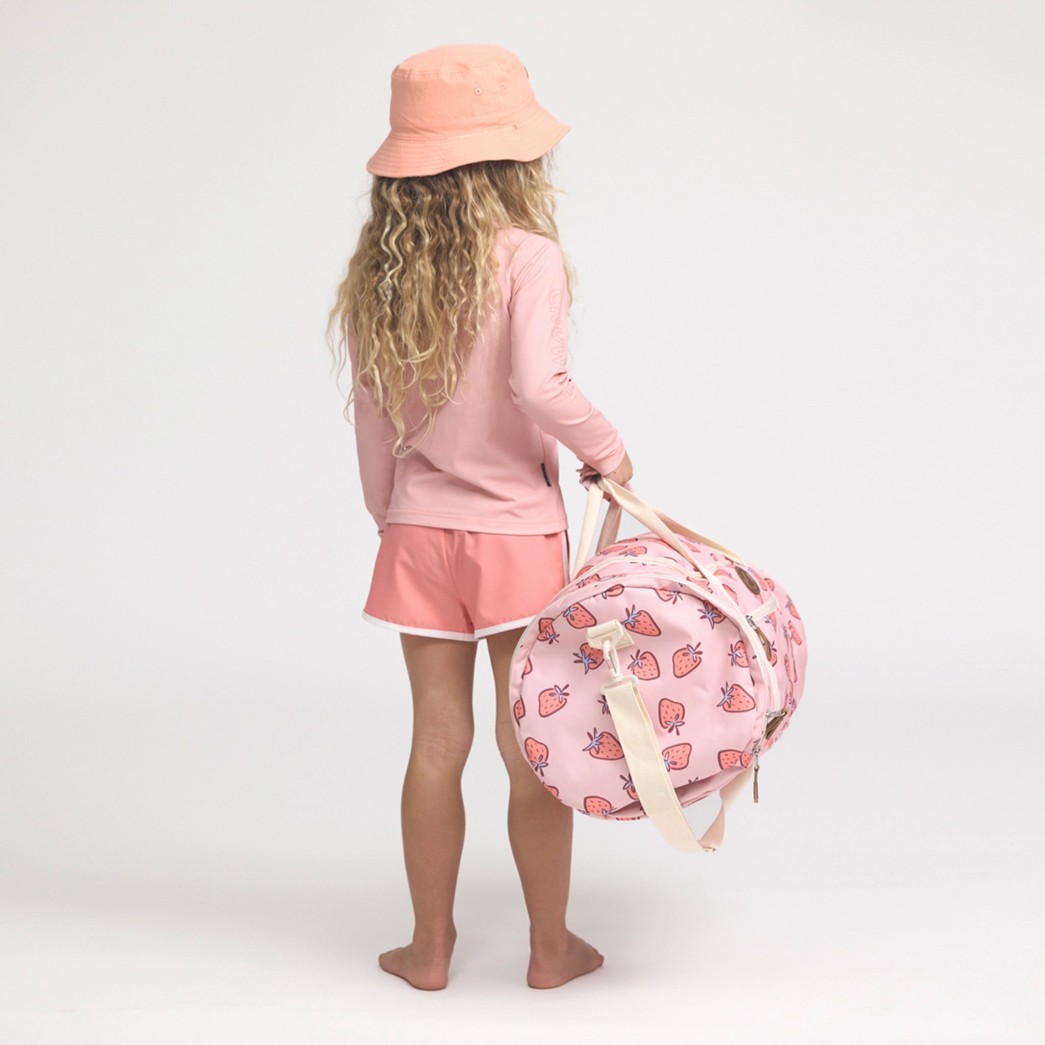Child holding a pink beach bag with strawberry pattern on a white background