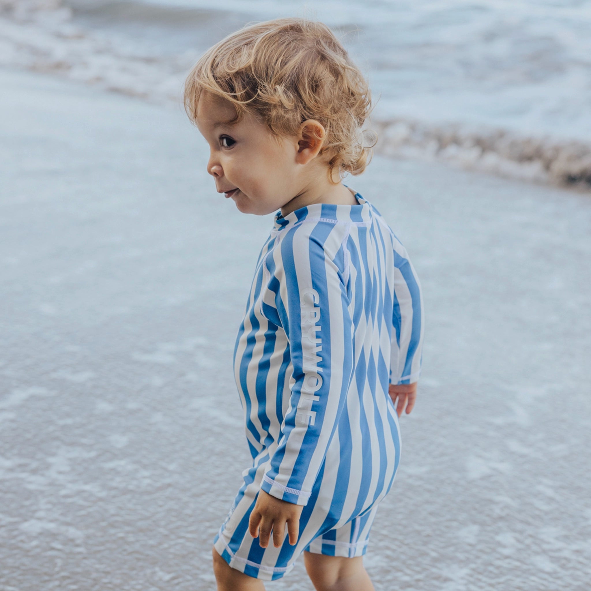Child wearing a blue and white striped swimsuit standing on a beach.