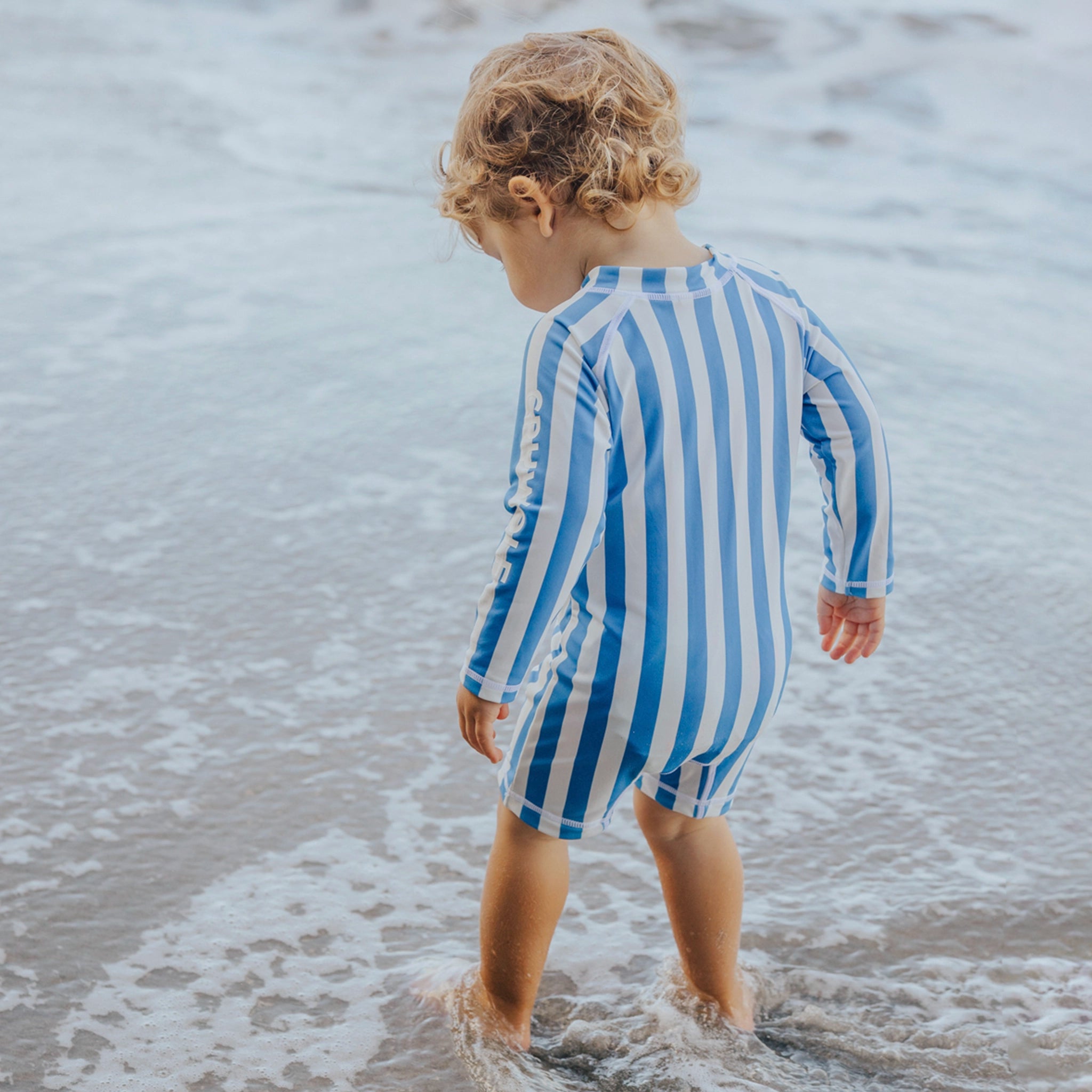 Child wearing a blue and white striped swimsuit walking on a beach.