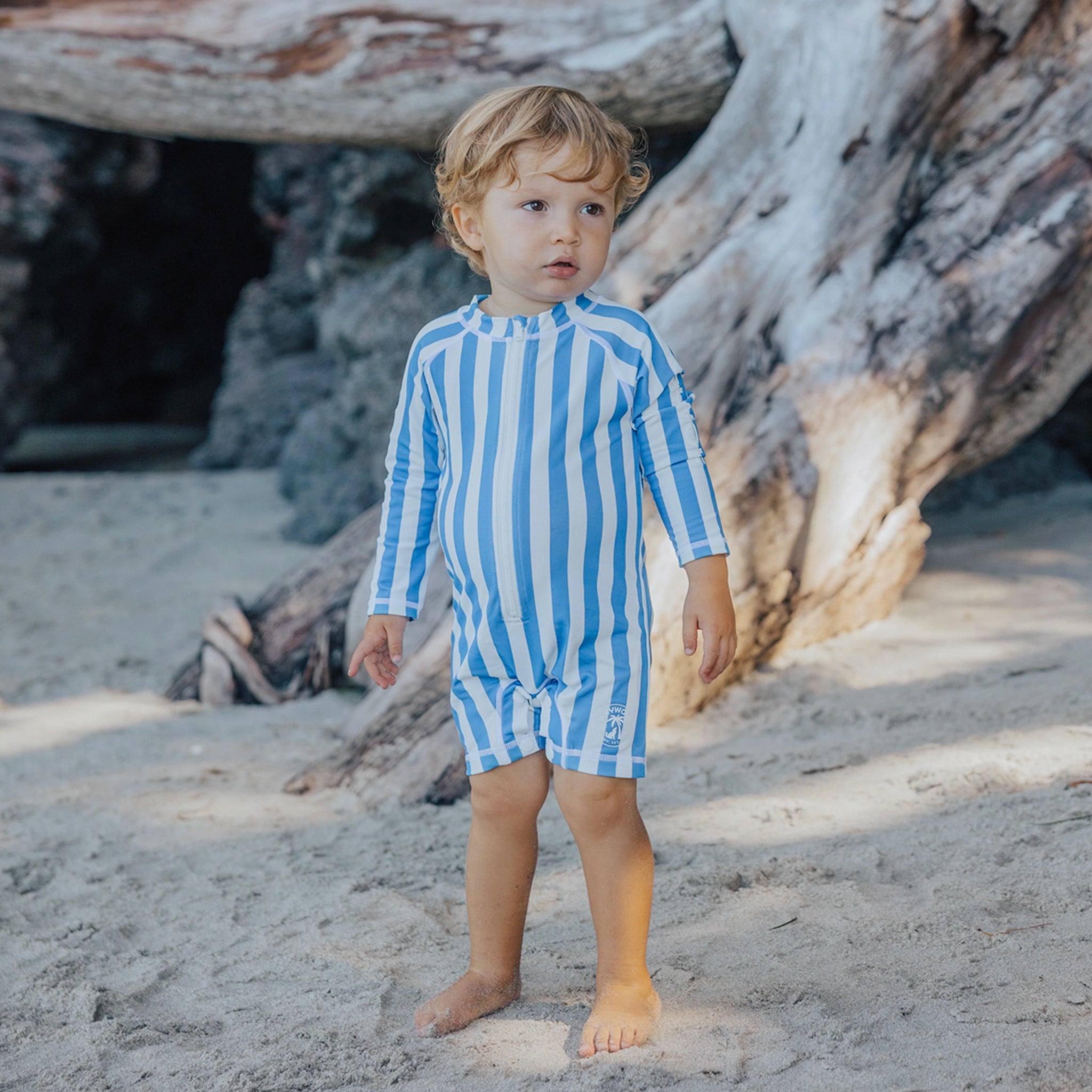 Child wearing a blue and white striped swimsuit on a sandy beach.