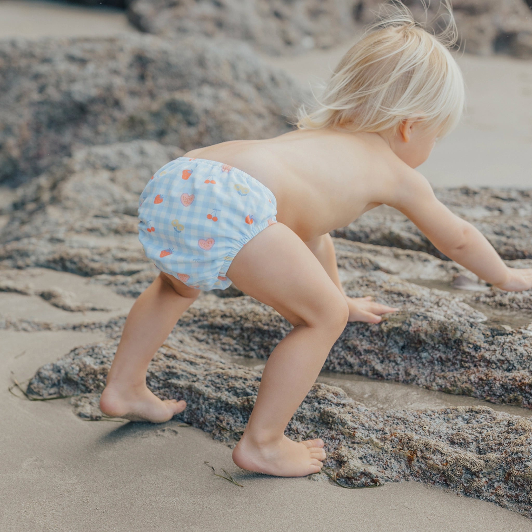 Toddler wearing a  blue and pink checkered swim nappy at the beach