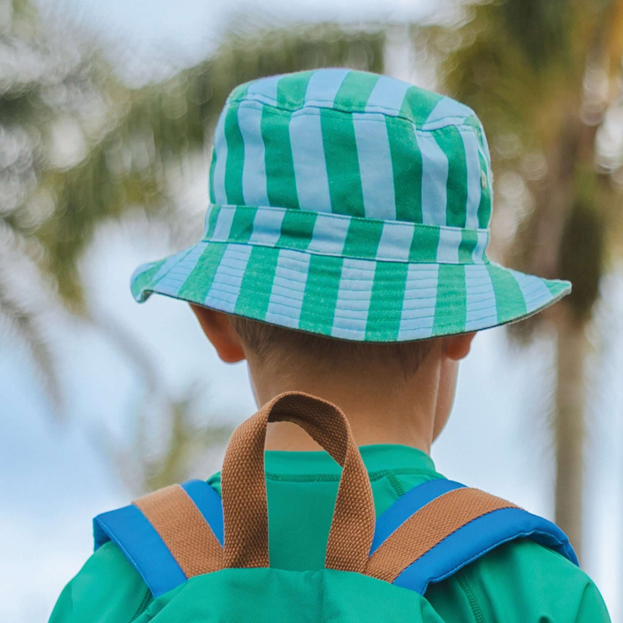 Child wearing Crywolf Reversible Bucket Hat - Deck Stripe with green and blue stripes, perfect for summer adventures.