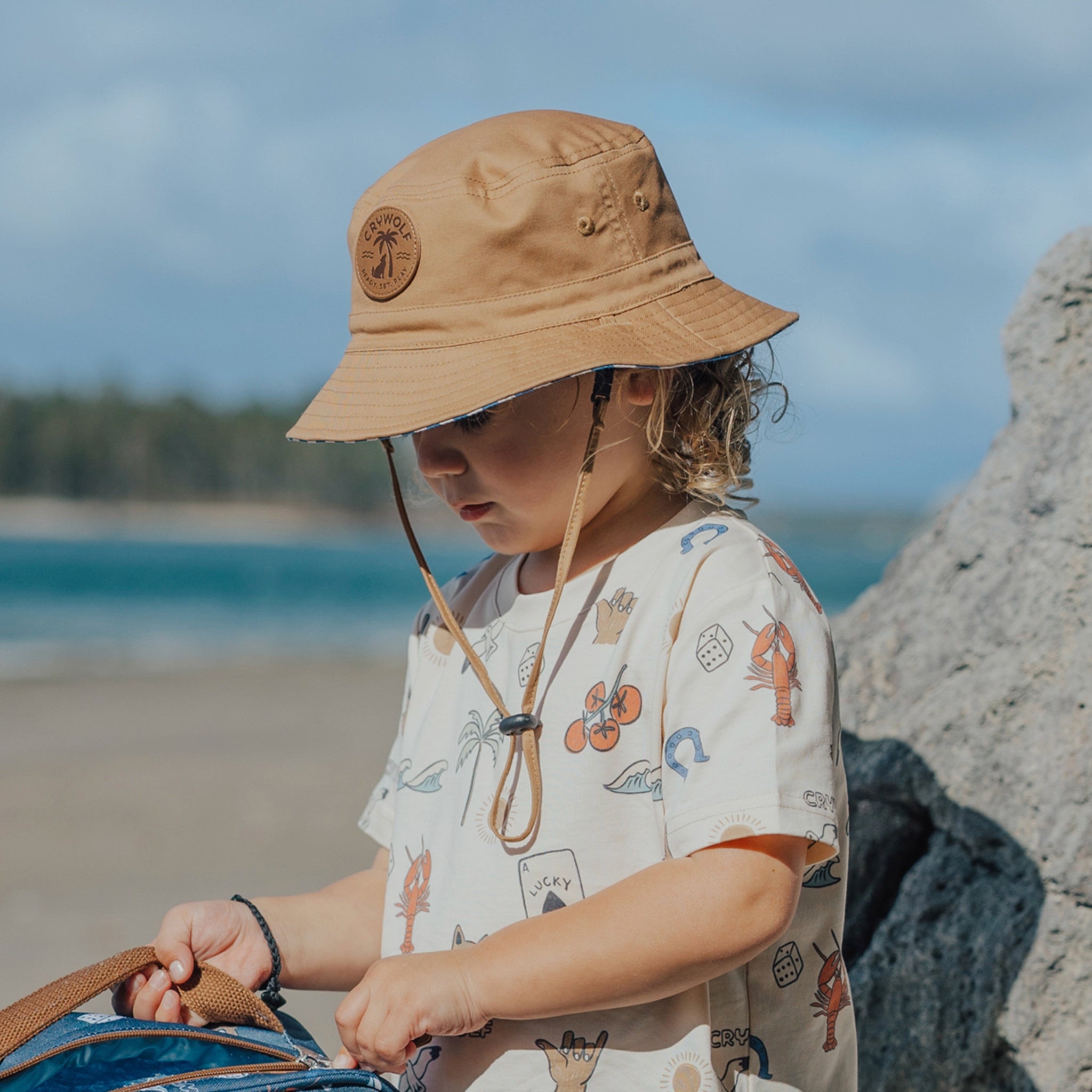 Child wearing a beige bucket hat with a logo on a beach