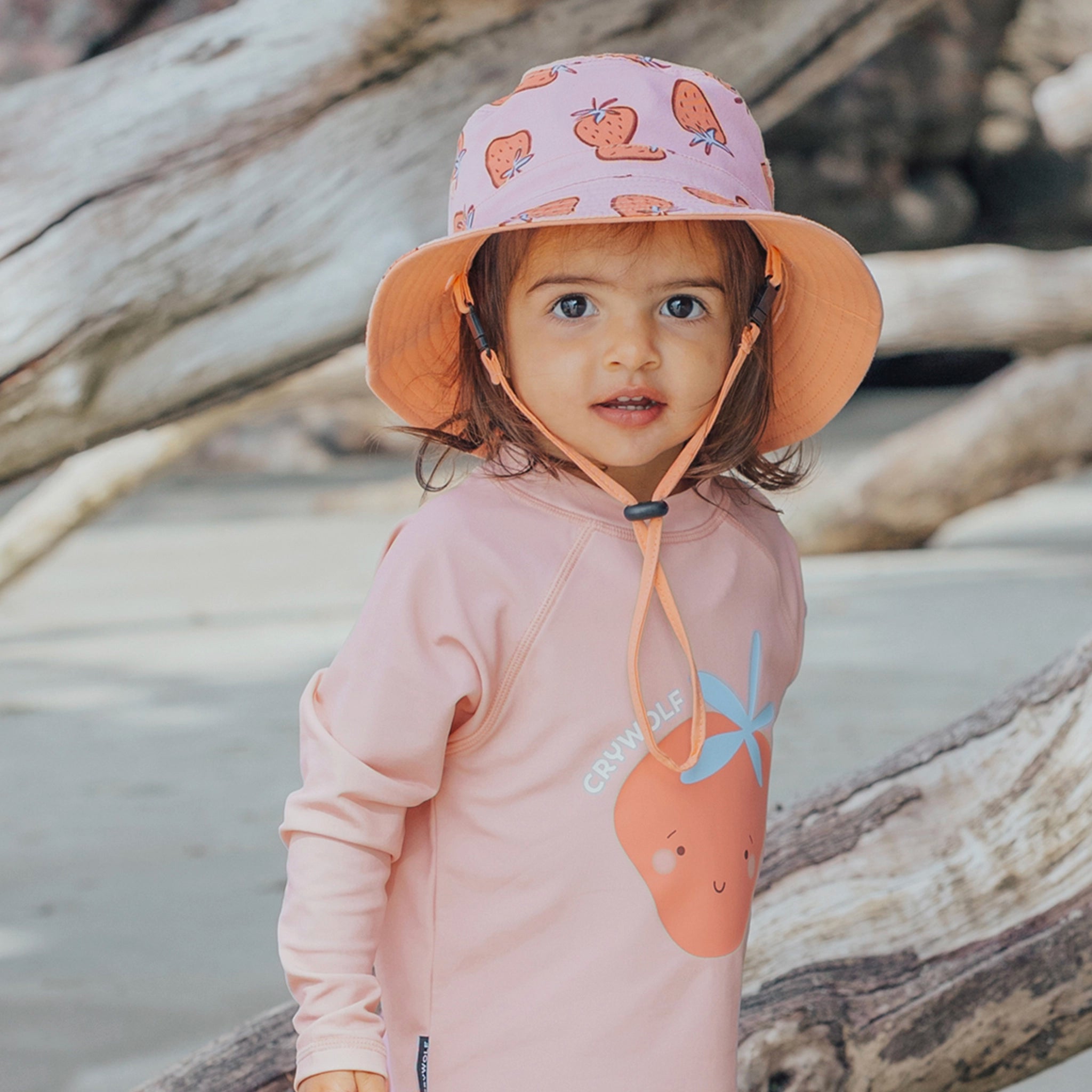Child wearing a pink hoodie and hat with carrot design on a beach