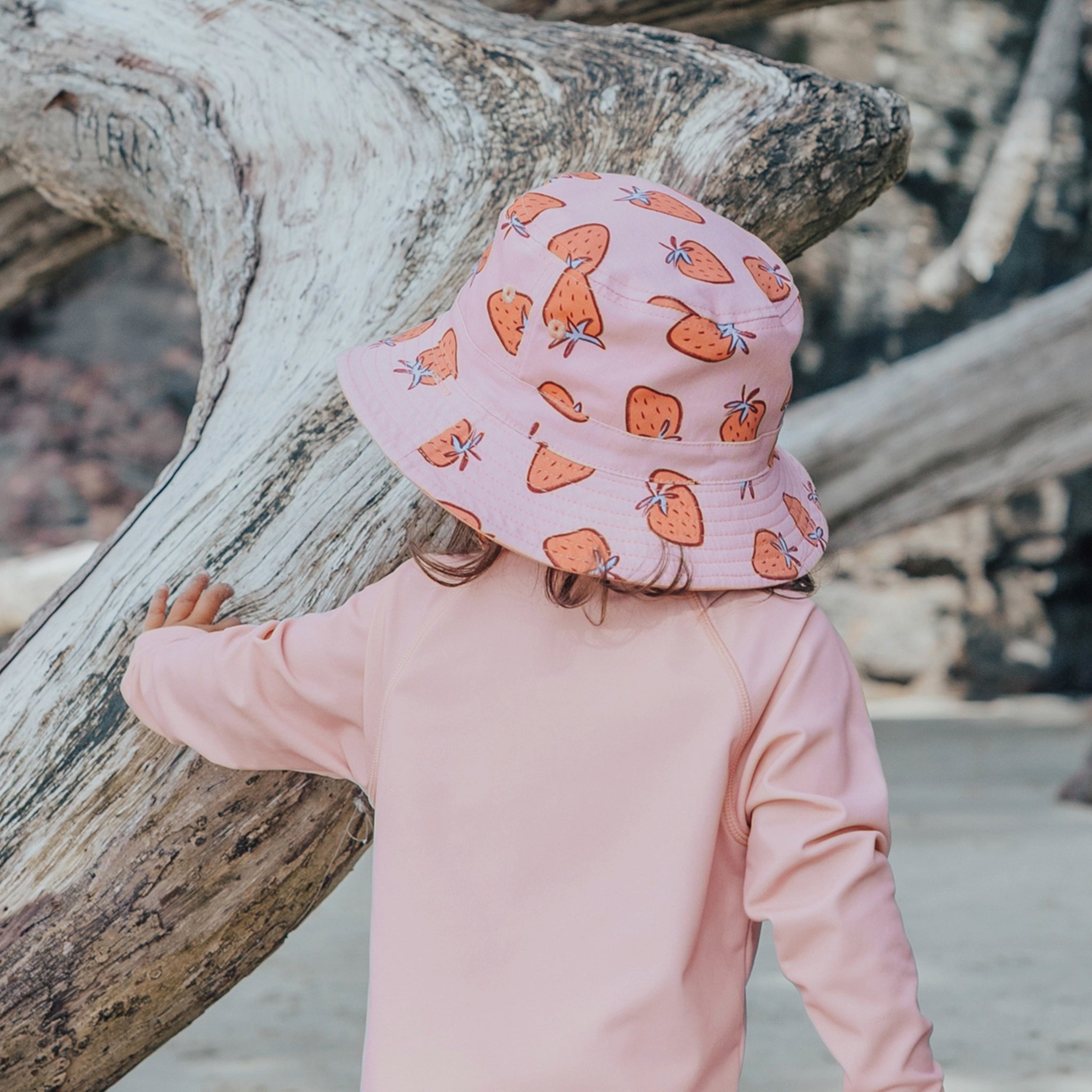 Child wearing a pink sun hat with orange patterns on a beach.