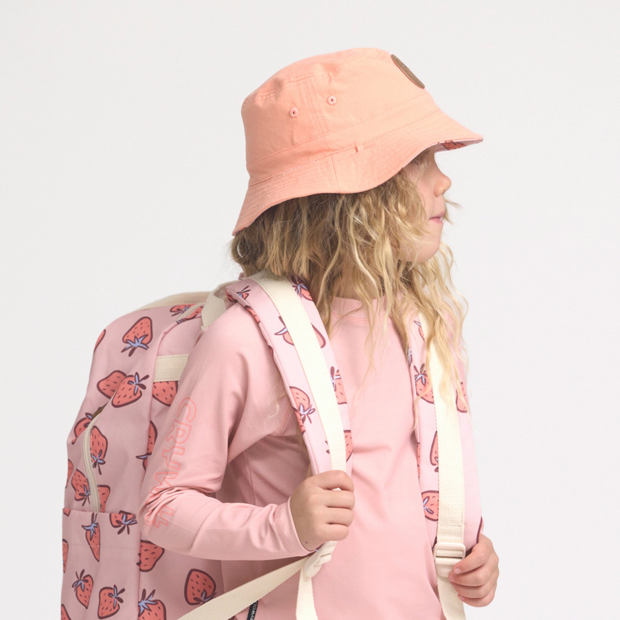 Person wearing a pink bucket hat and carrying a pink backpack with strawberry pattern on a light gray background