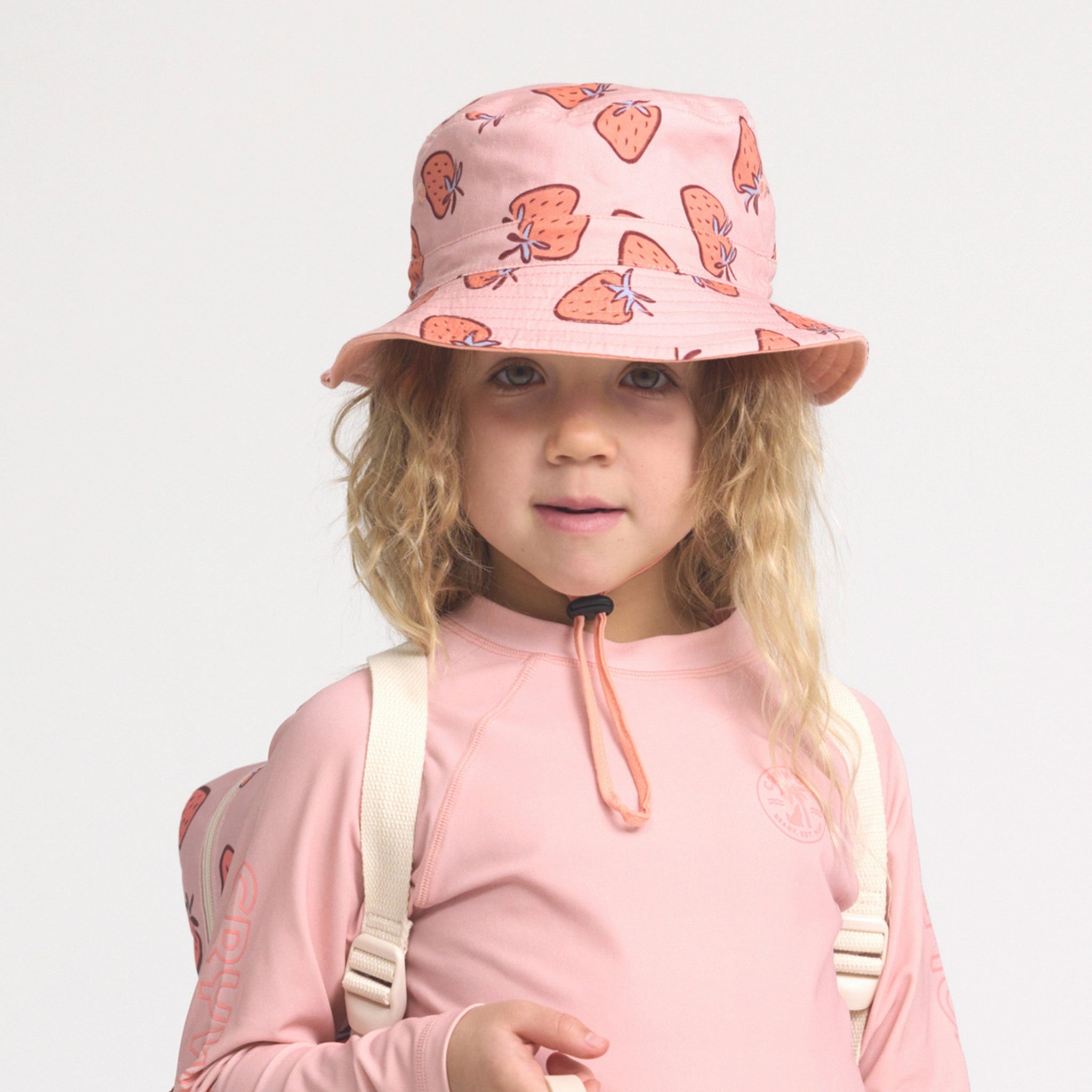 Child wearing a pink bucket hat with strawberry pattern on a light gray background