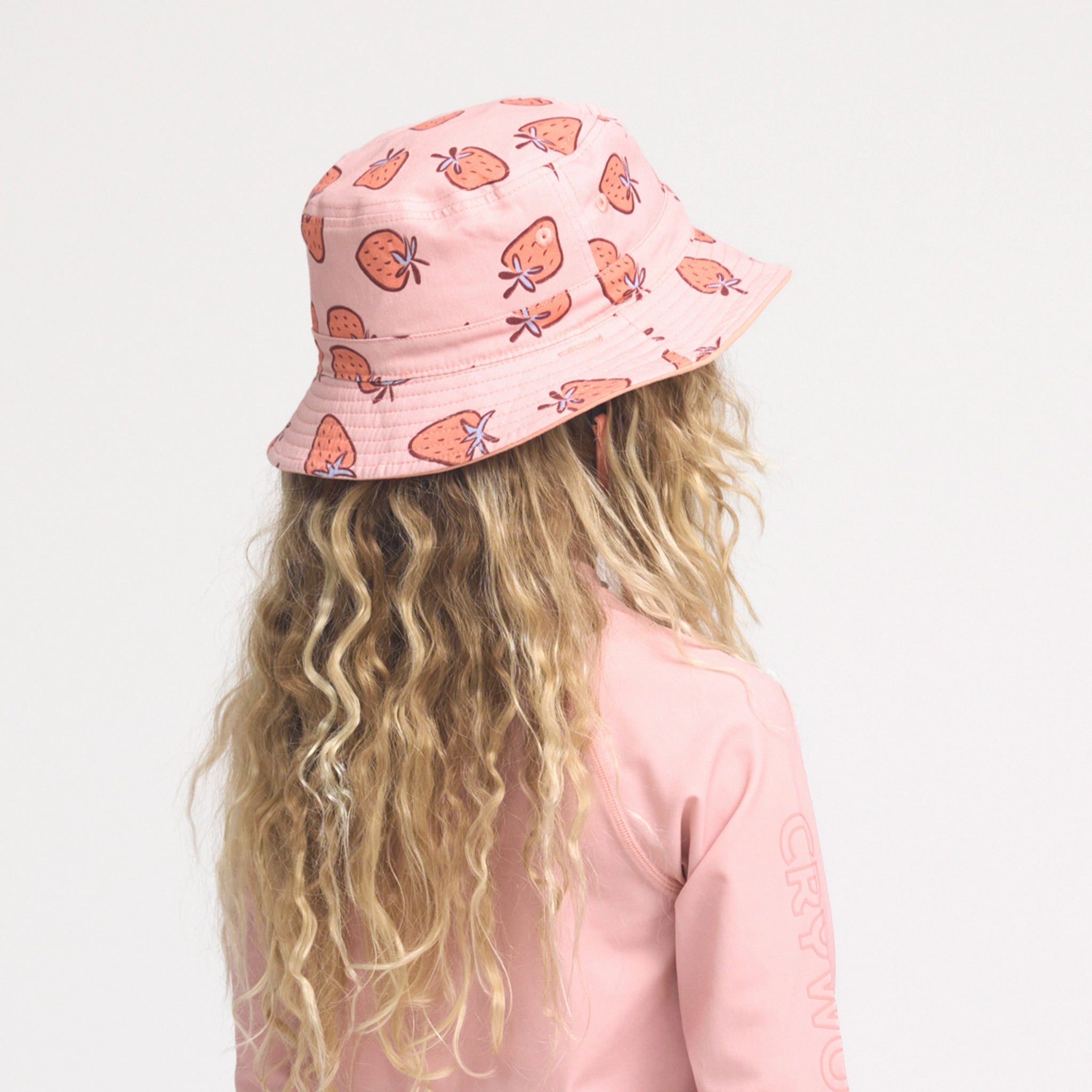 Person wearing a pink bucket hat with butterfly pattern on a plain background