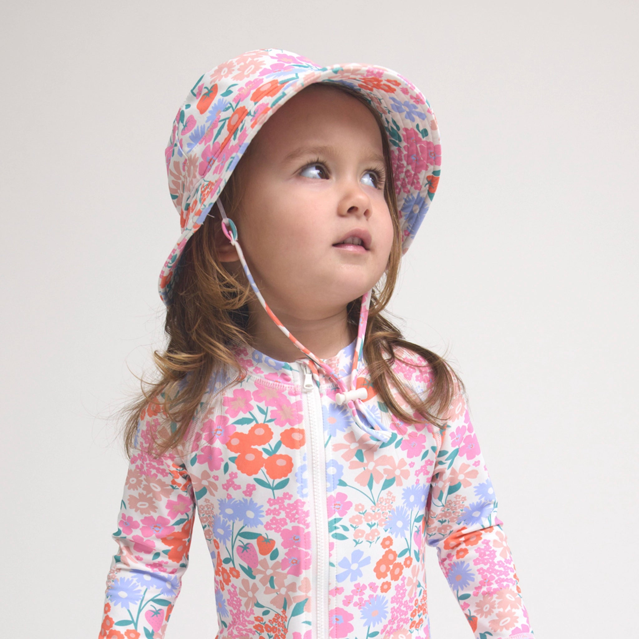 Child wearing a floral sun hat and matching outfit on a plain background