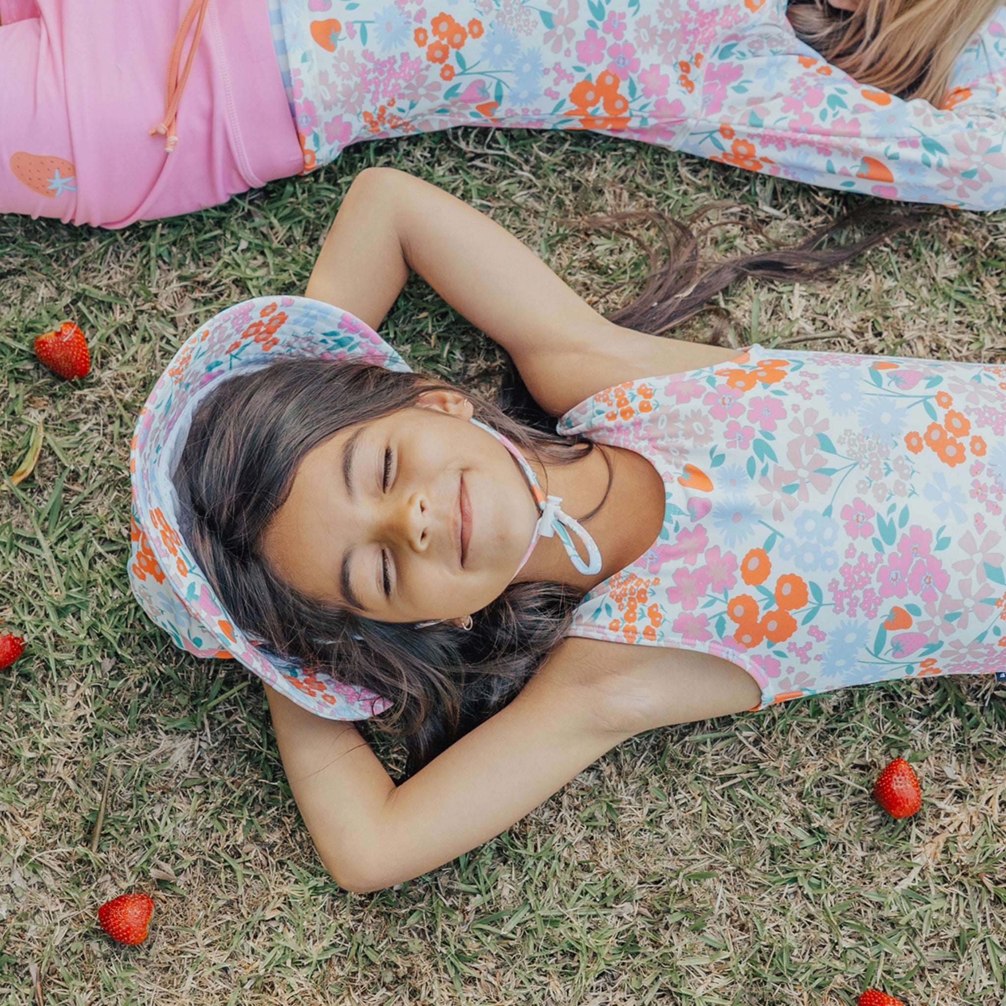 Young girl in a floral dress lying on grass with strawberries around
