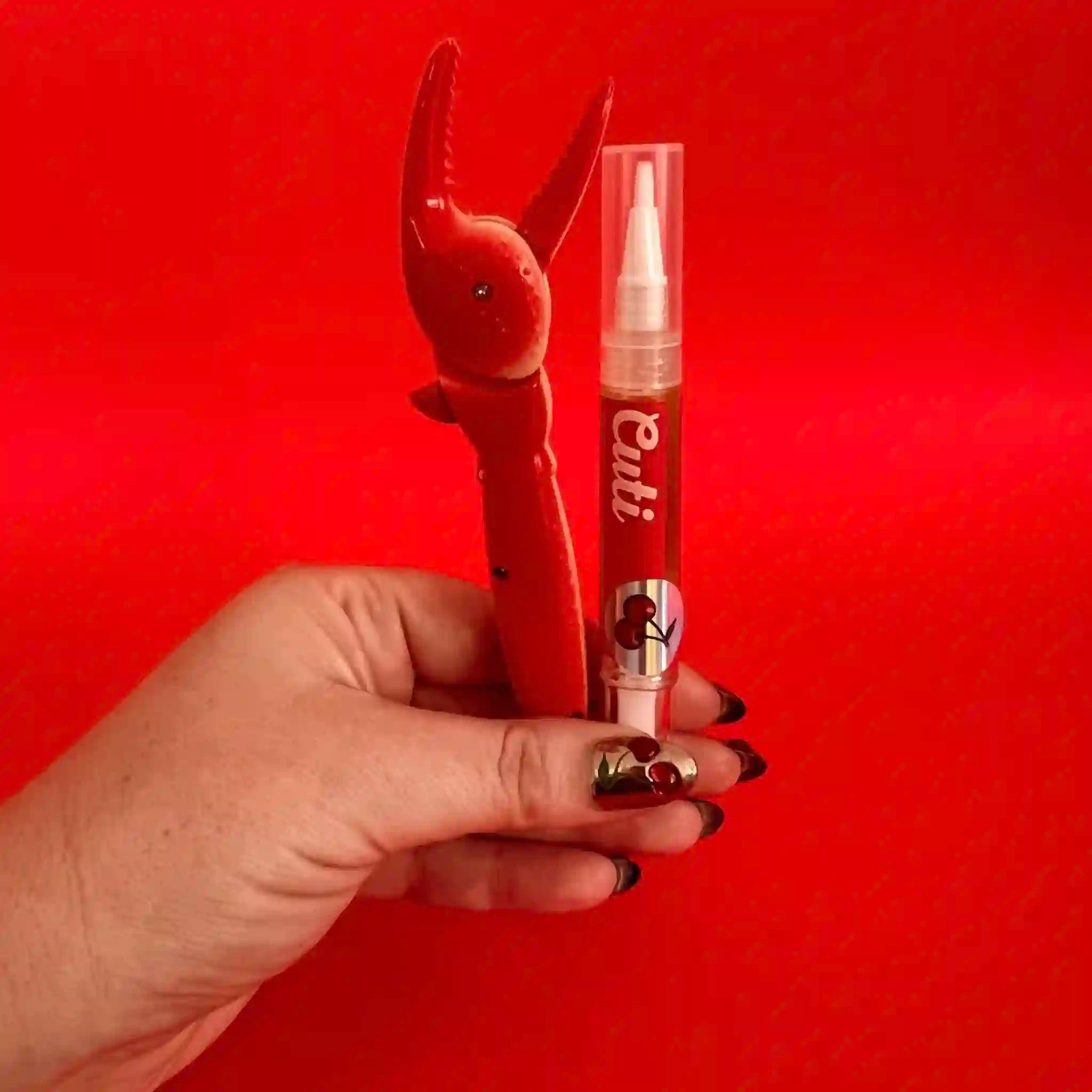 Hand holding a novelty cuticle pen shaped like a lobster against a red background
