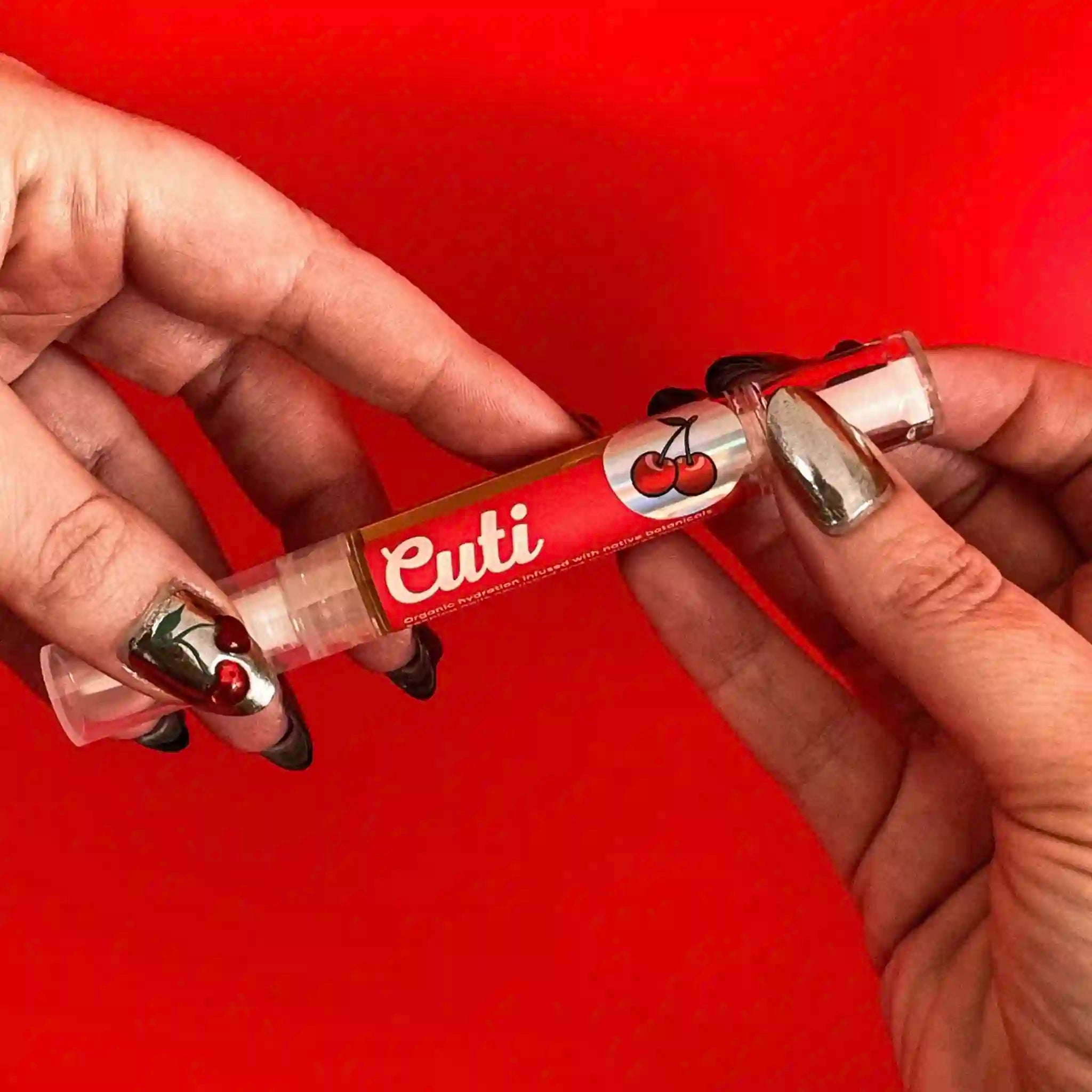 Hand holding a red and white 'Cuti' cuticle oil applicator against a red background