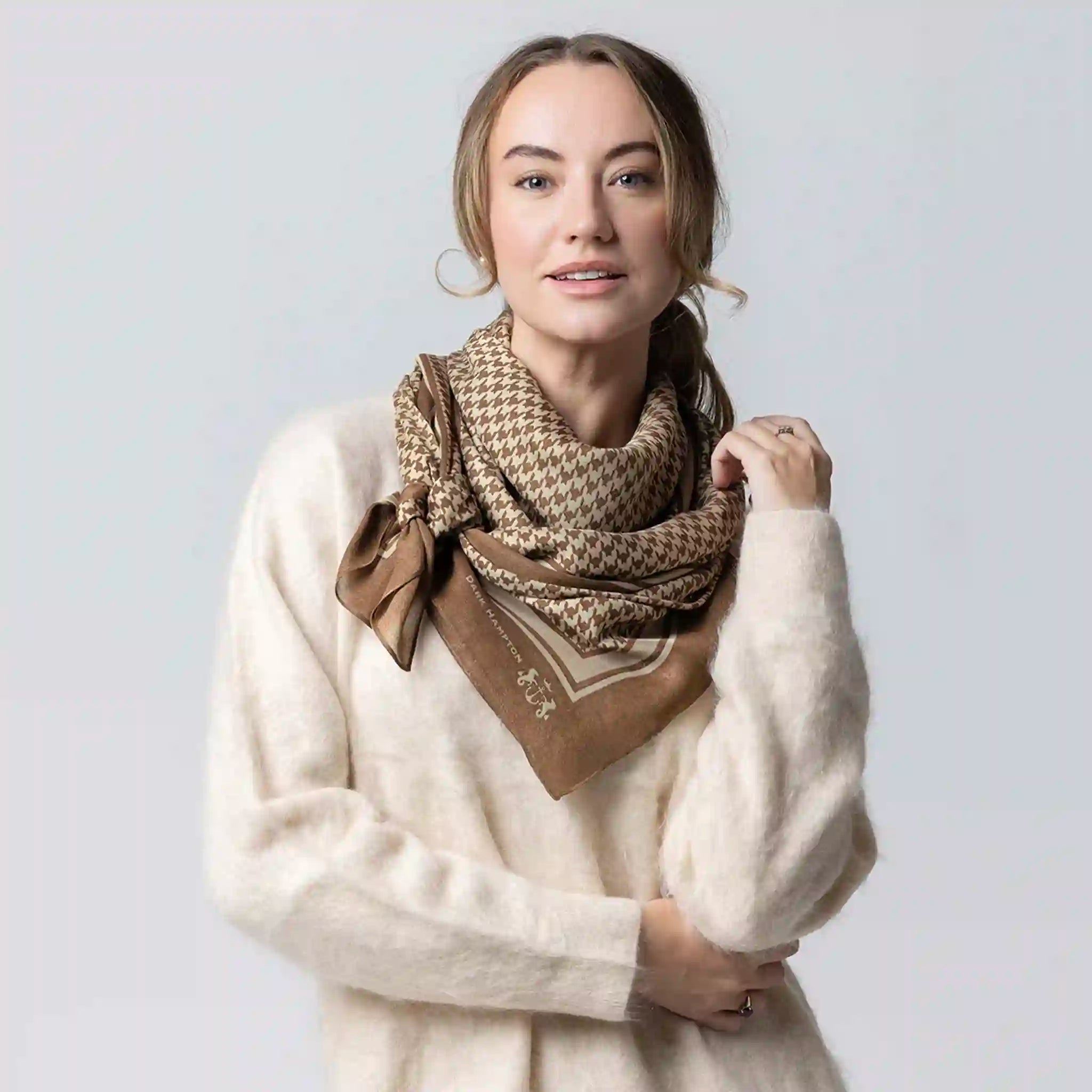 Woman wearing a beige scarf with a patterned design on a plain background