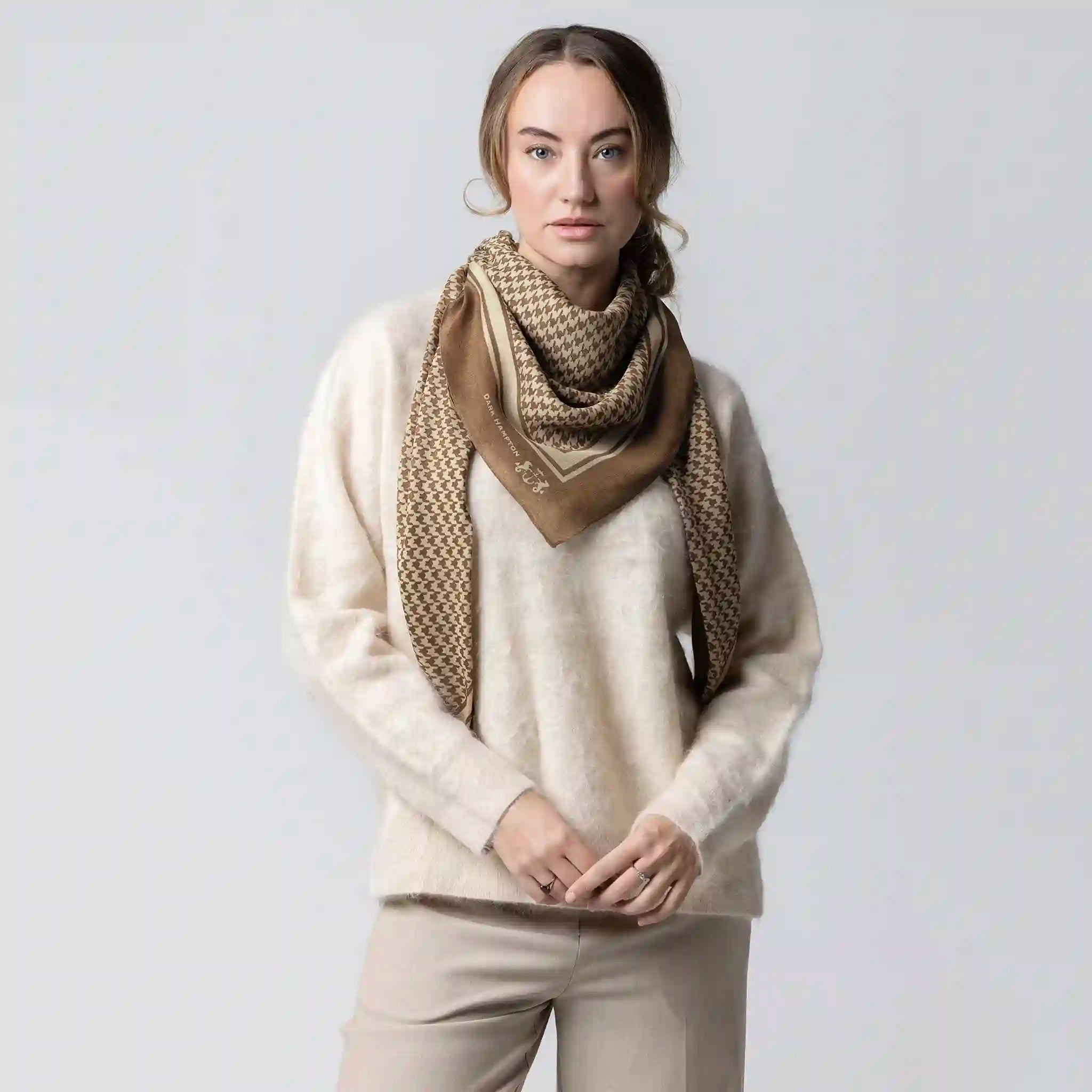 Woman wearing a beige sweater and patterned scarf against a plain background