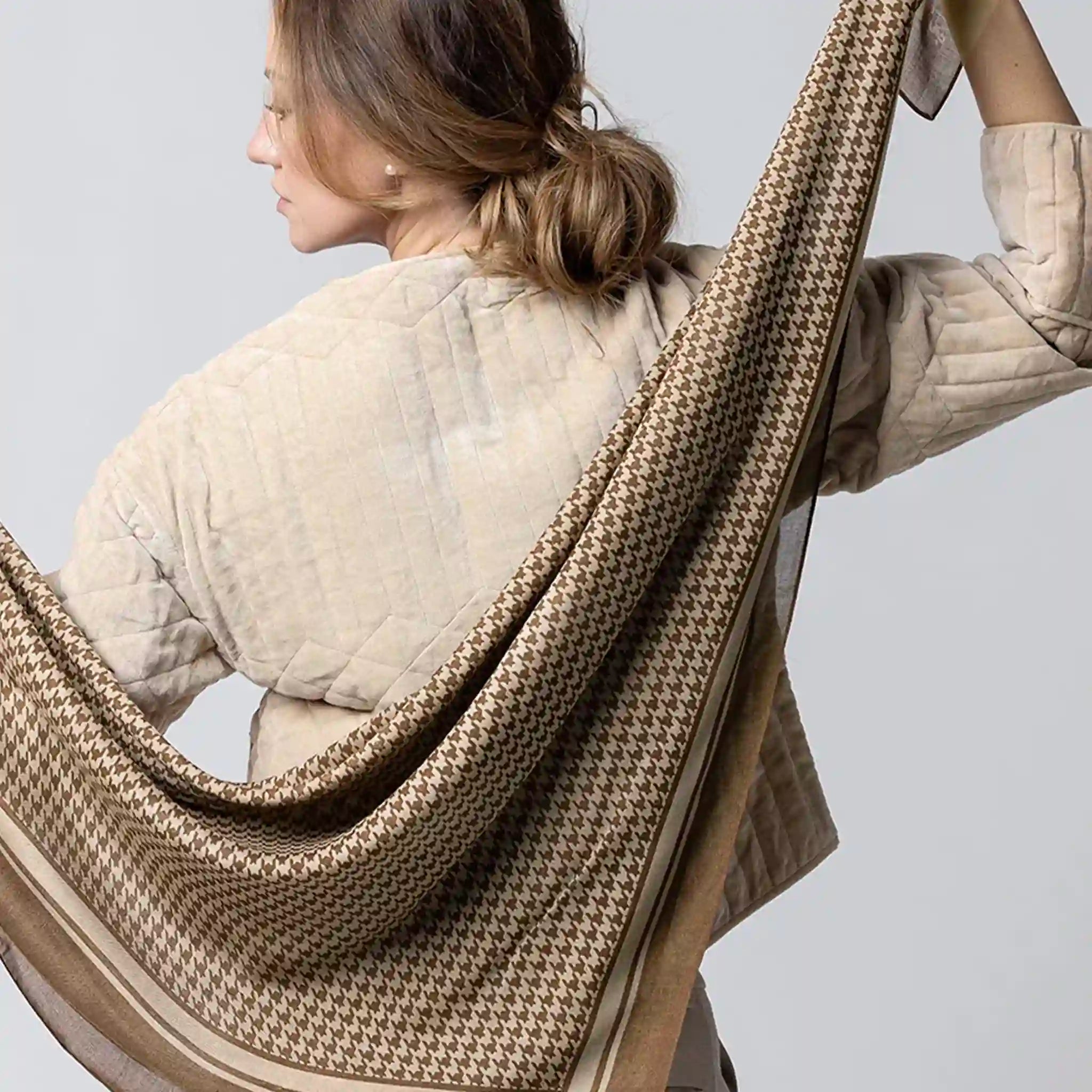 Person wearing a beige quilted jacket with a houndstooth patterned scarf draped over their shoulders against a light gray background.