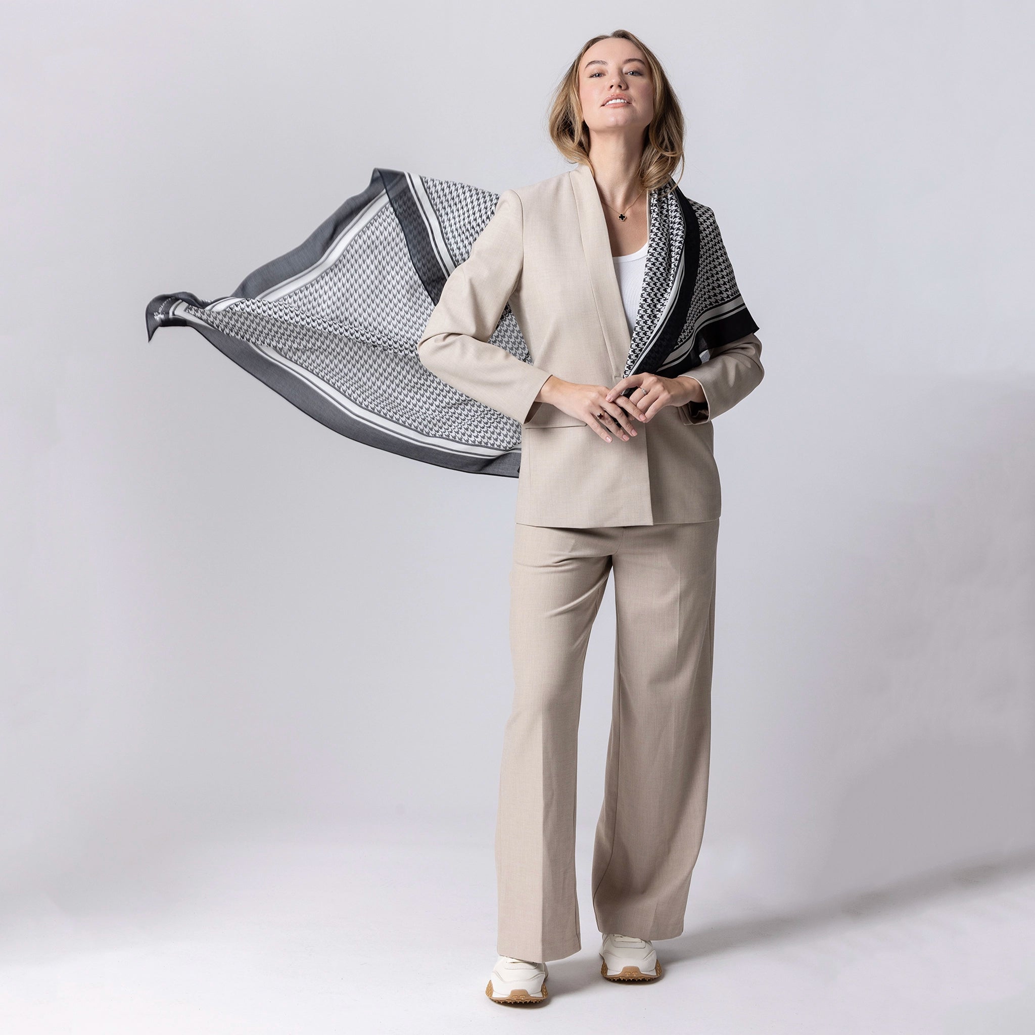 Woman in a beige suit holding a patterned scarf against a white background