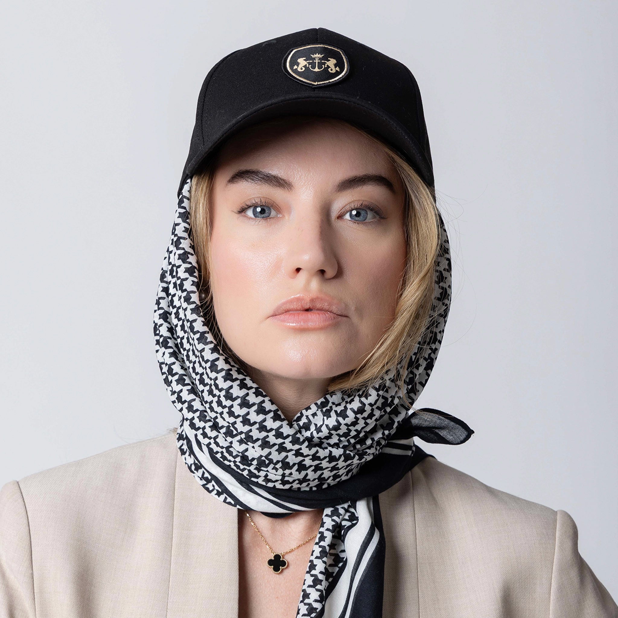 Person wearing a black cap with a logo and a black and white patterned scarf on a light gray background