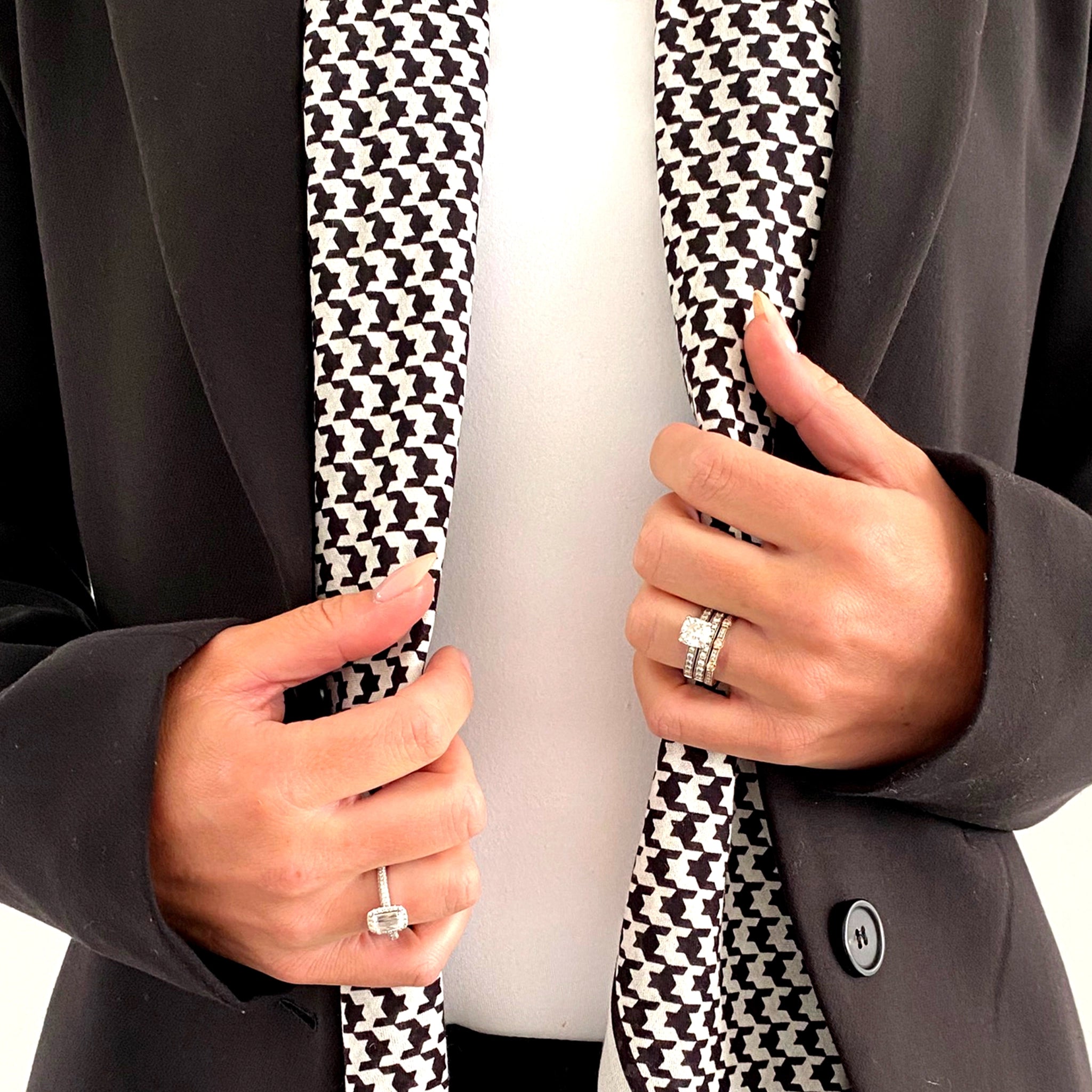 Person wearing a black coat with a houndstooth pattern tie, holding it with both hands.