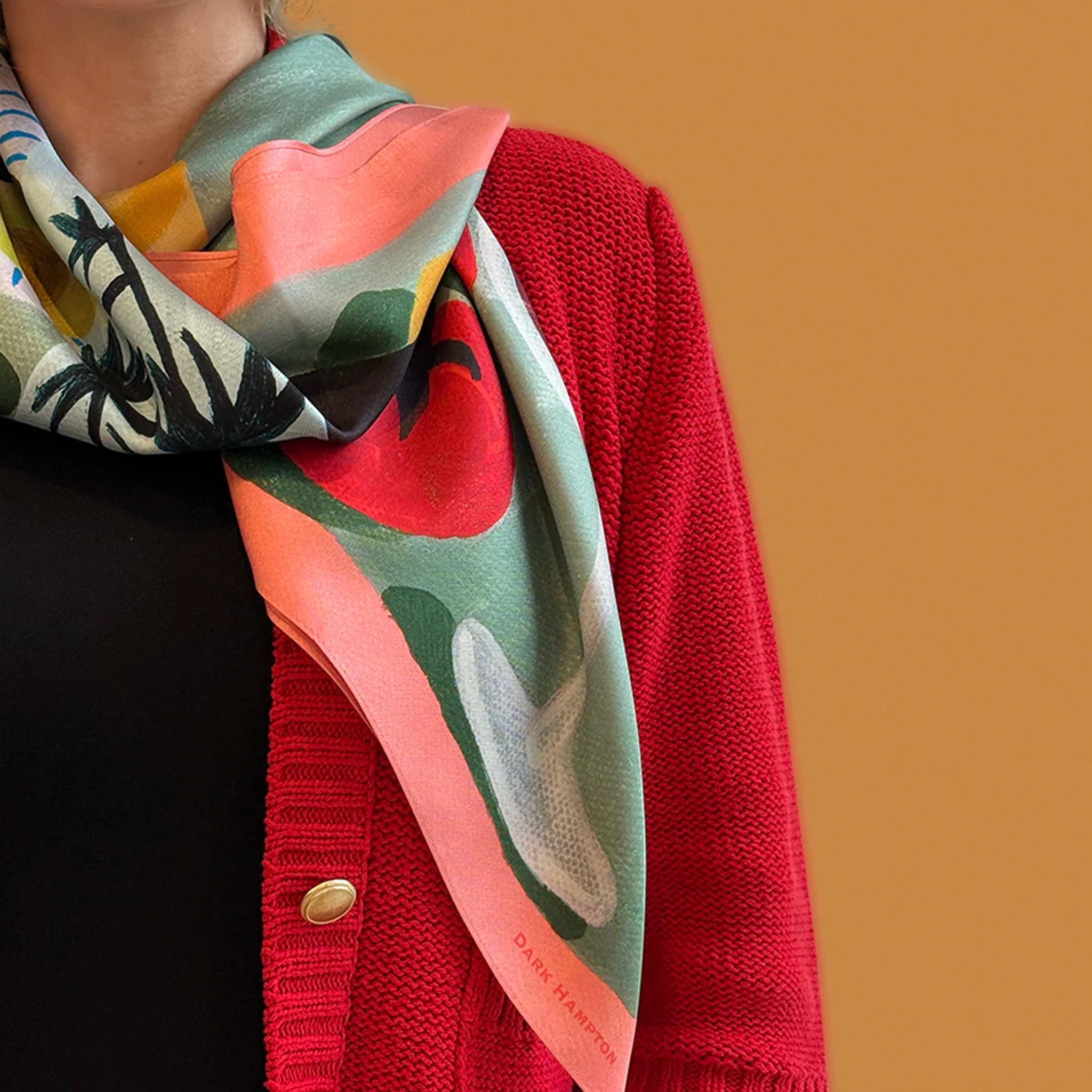 Person wearing a colorful scarf with a red sweater on a brown background