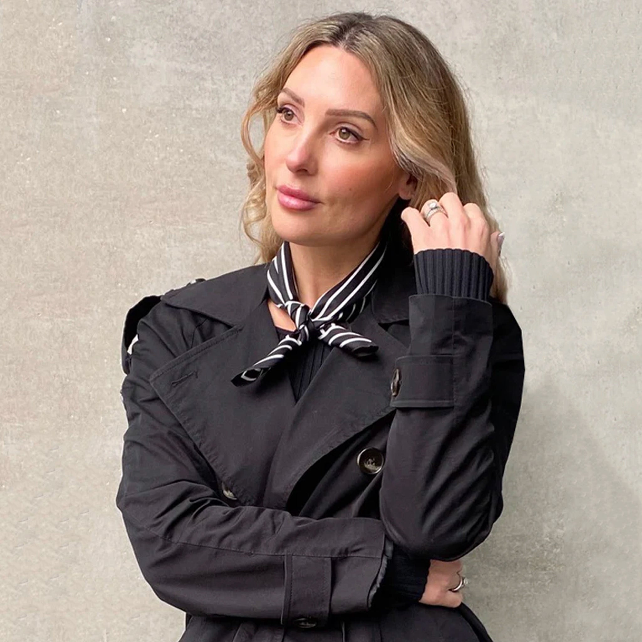 Woman wearing a black coat with a striped scarf against a neutral background