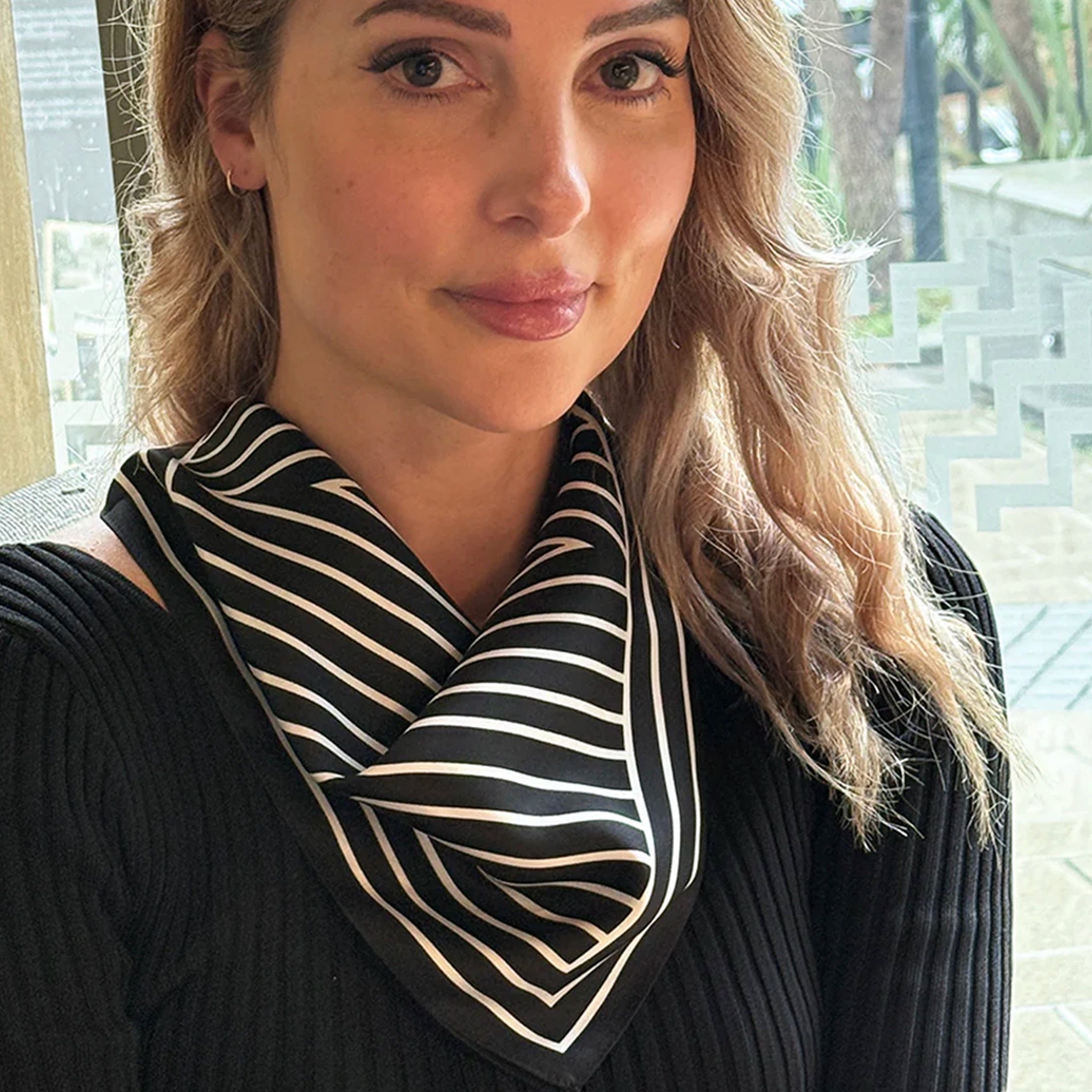 Woman wearing a black and white striped scarf with a blurred outdoor background